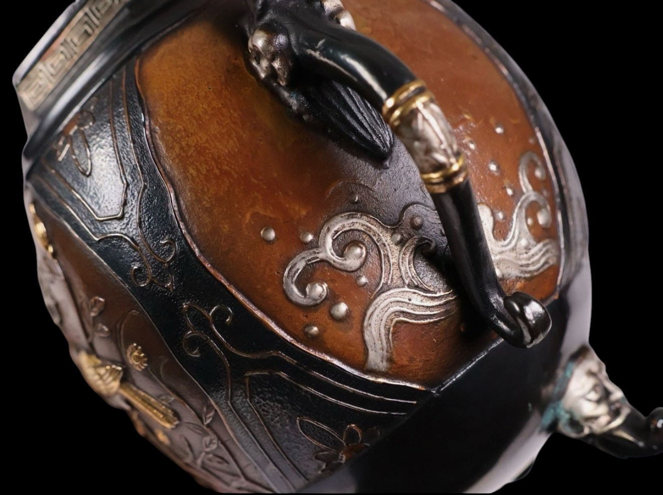 Close-up angled view of a Takaoka bronze koro, showing Kirin and dragon motifs with shimmering precious-metal inlay katana