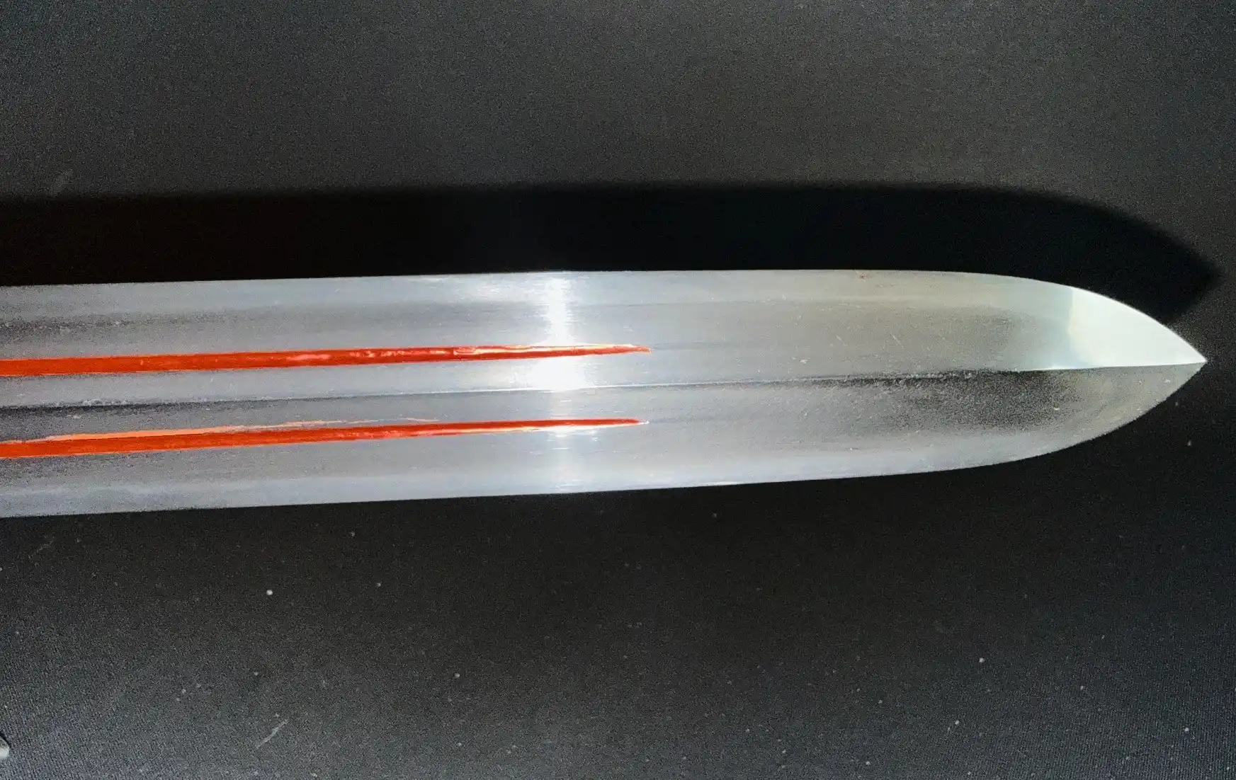 Close-up of Ōmi Yari Sukekiyo Naginata tip with shiny surface, red details on black background