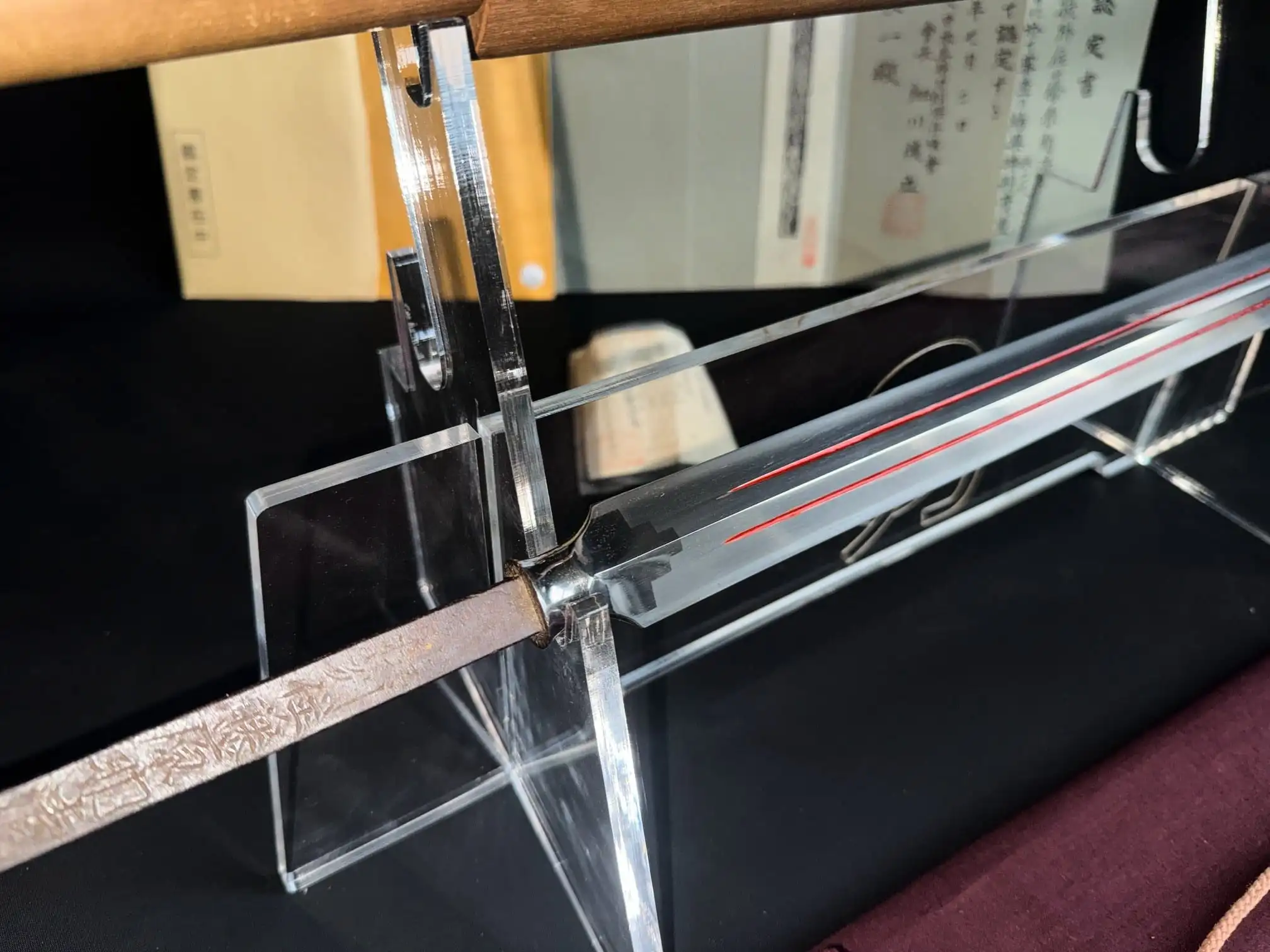 Close-up of Ōmi Yari Sukekiyo Naginata blade with red grooves and rusted tang displayed on clear stand