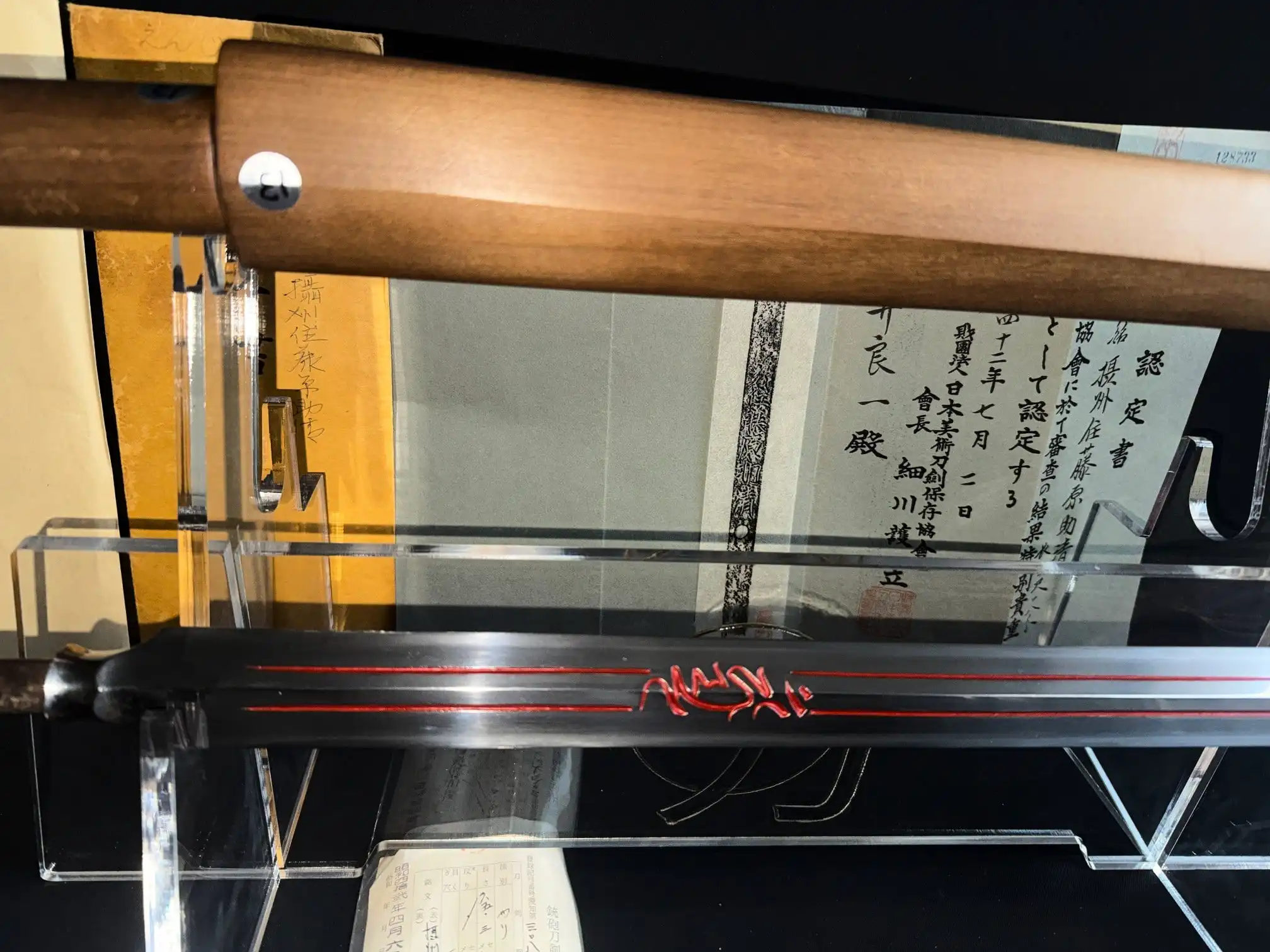 Closeup of the Ōmi Yari Sukekiyo Naginata blade with red hi carving, displayed on a stand.