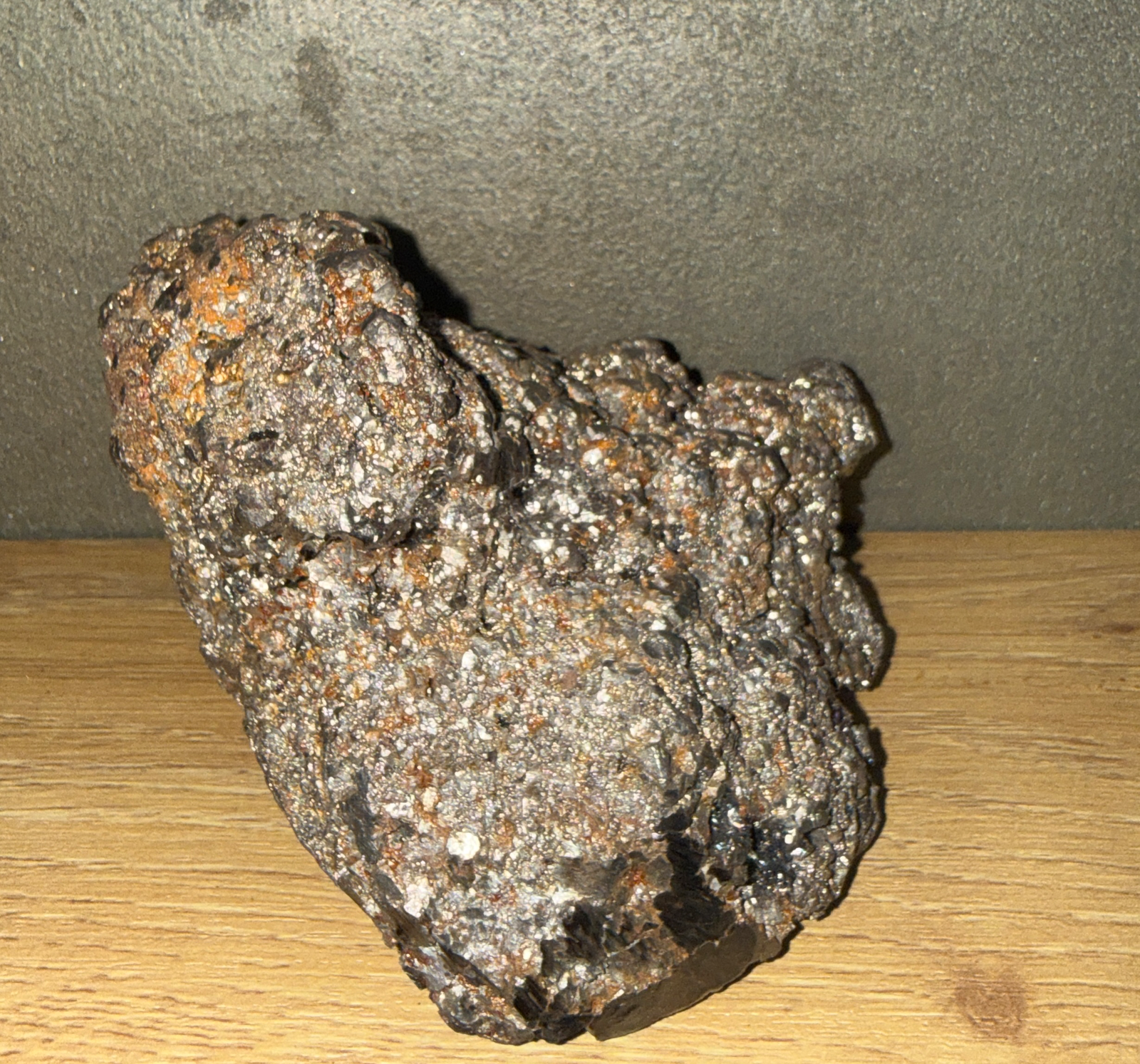 Rough-textured Japanese Tamahagane Steel accessory with silvery, dark, and orange fragments on a wooden surface