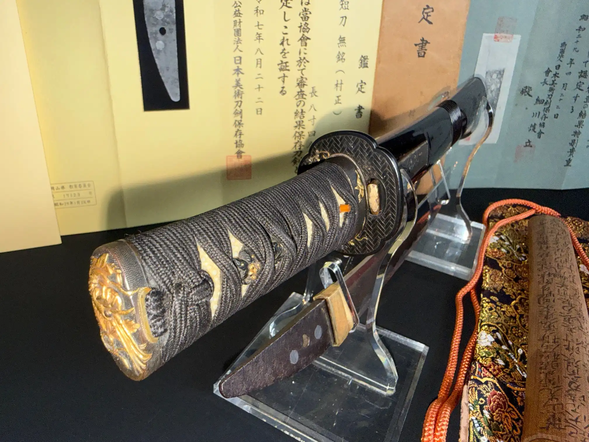 Nidai Muramasa Sayagaki Katana, displayed on a stand with paperwork, showing intricate hilt and blade details.