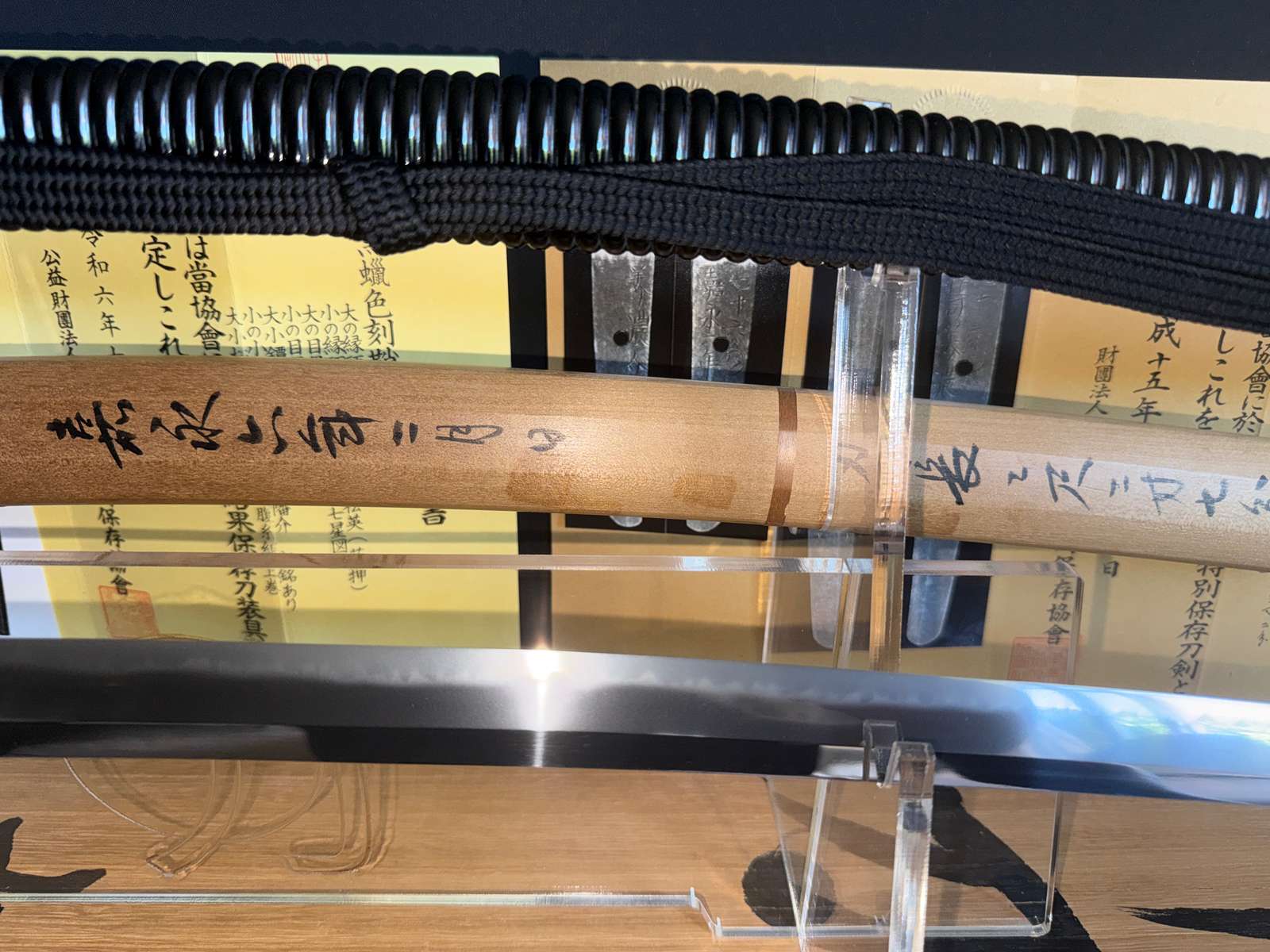 Close-up of a Naotane's Final Known Daishō katana, showing the blade's hamon and an inscribed wooden scabbard.