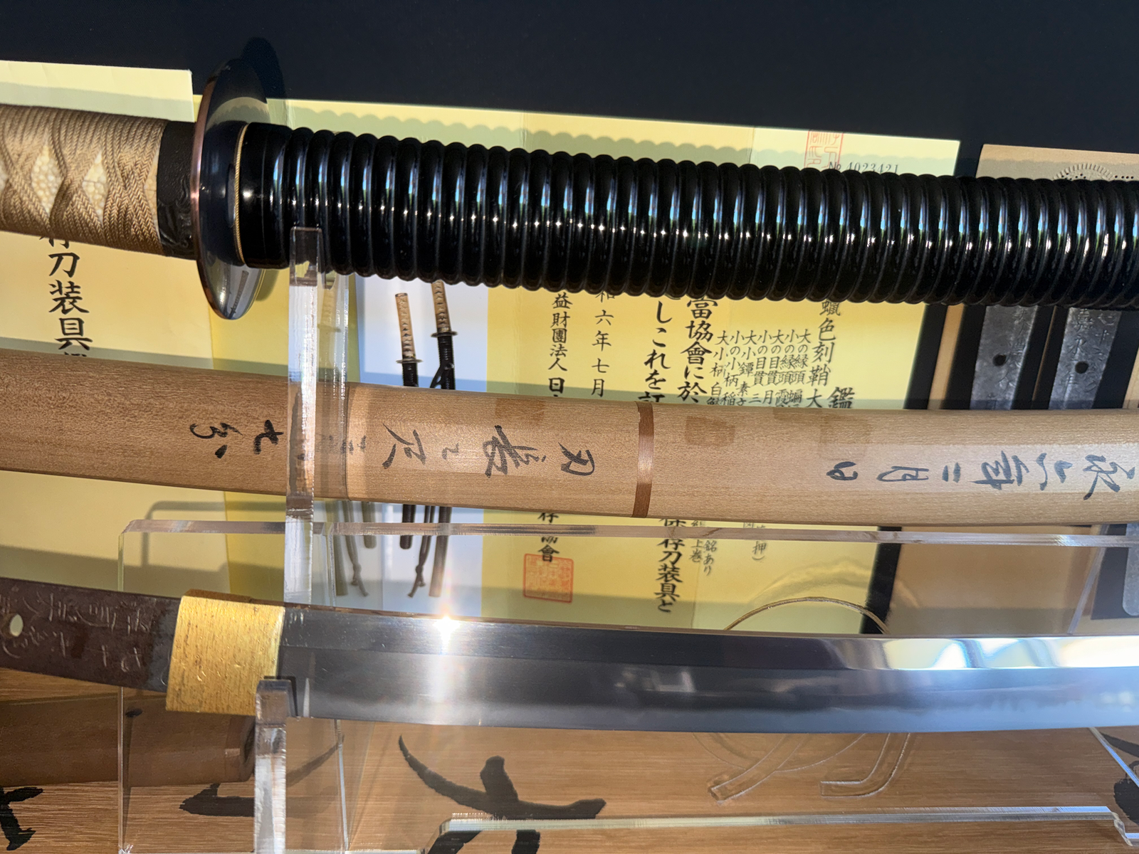 Naotane’s Final Known Daishō katana, with highly polished blade, black lacquer saya, and tsuba on display.