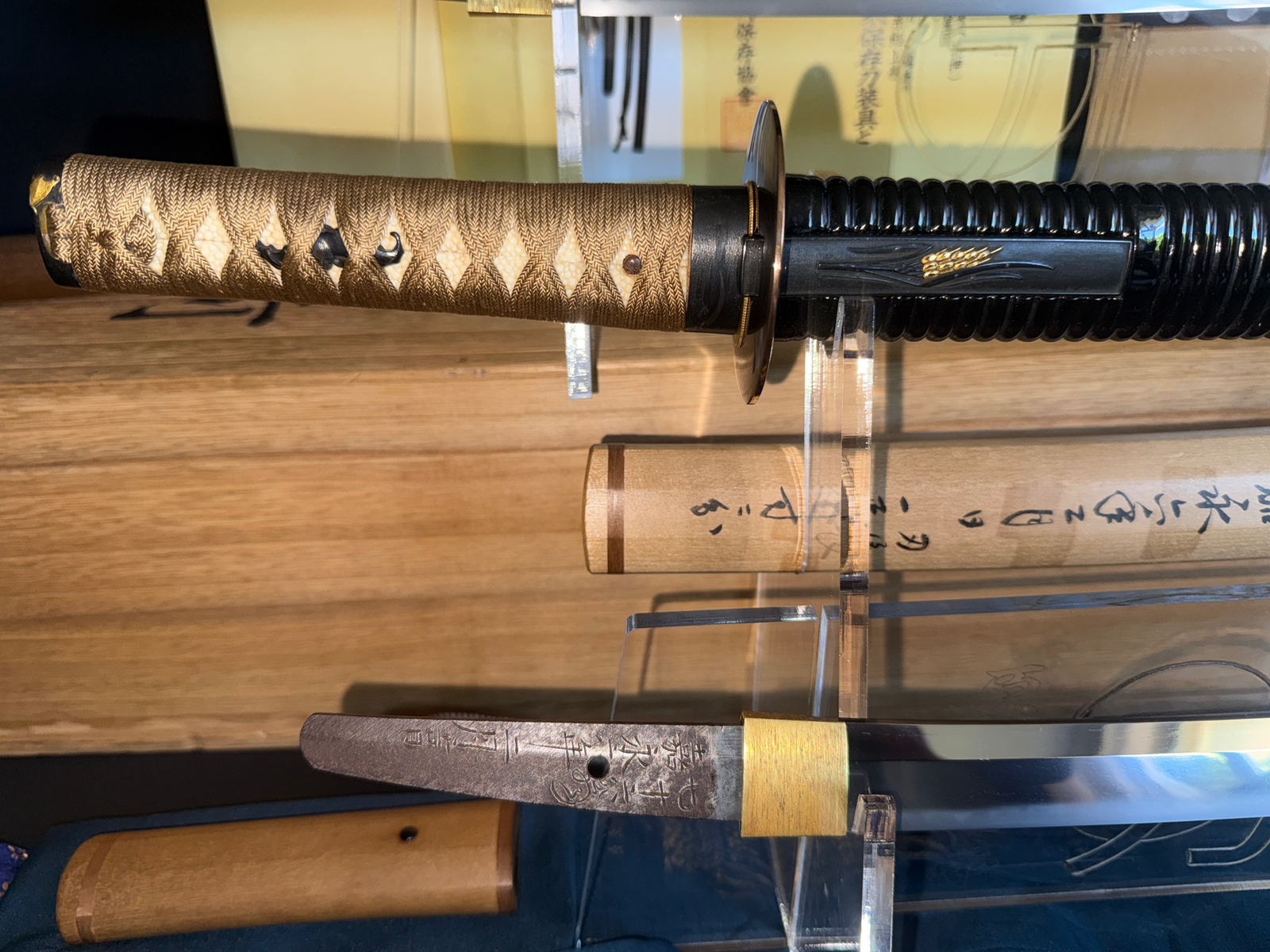 Close-up of a Naotane's Final Known Daishō katana grip and a section of the blade, displayed on stands.