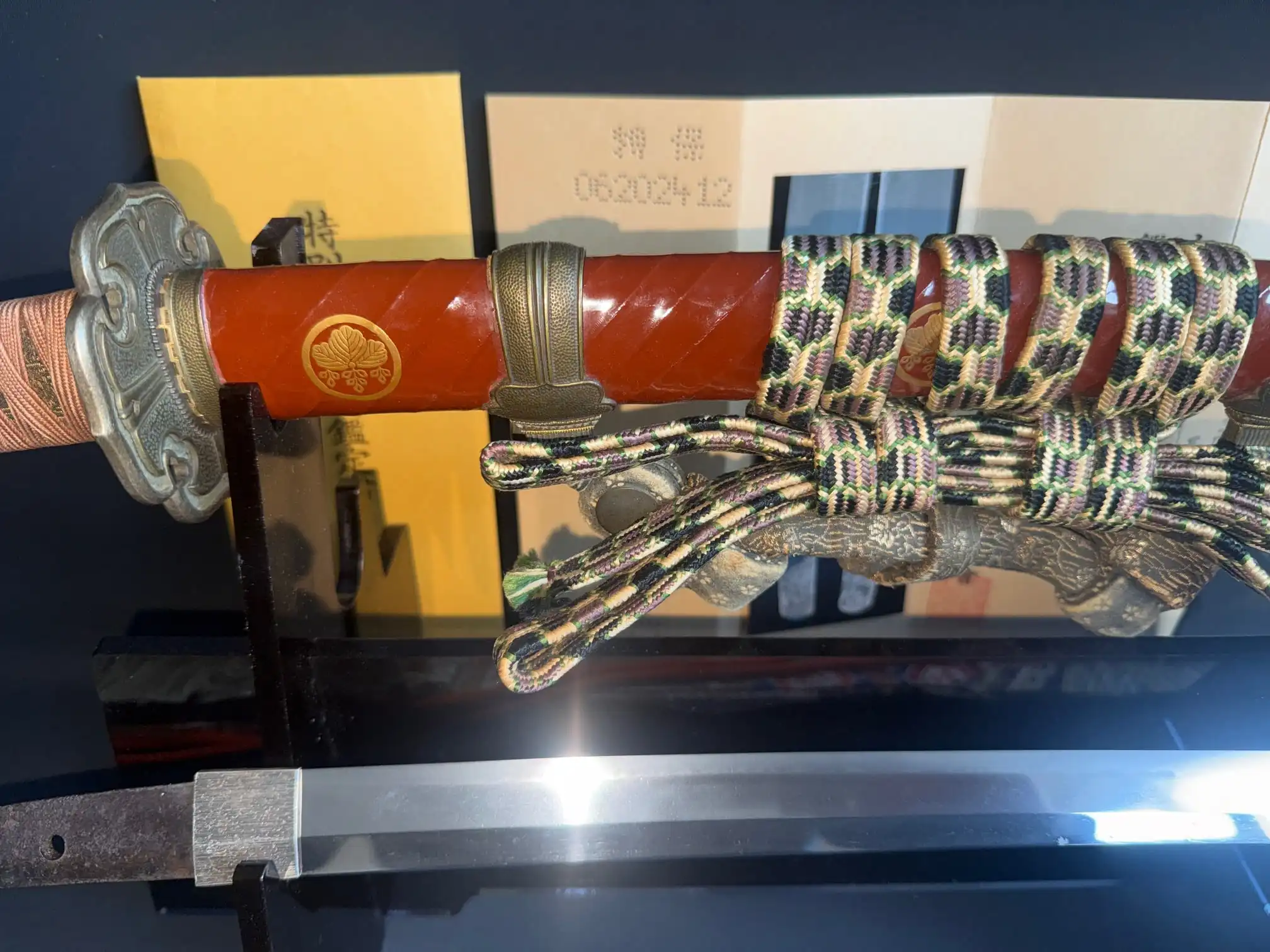 Horizontal shot of Nanbokuchō Tachi Hidemitsu katana with red saya, partially visible blade, and braid accents
