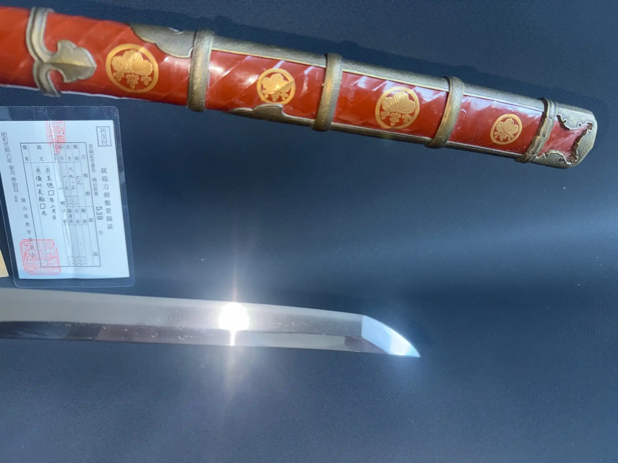 Close-up of a Nanbokuchō Tachi Hidemitsu katana with red scabbard and paperwork