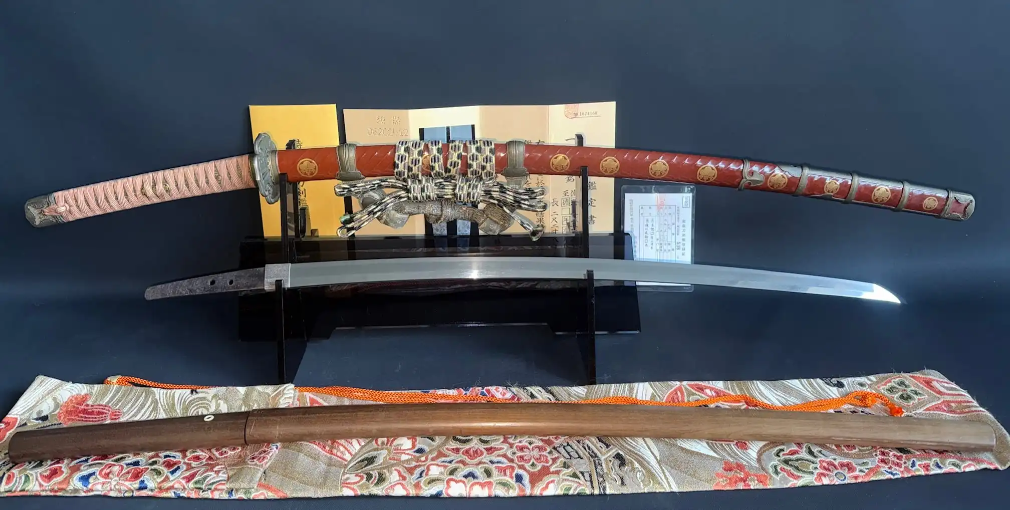 Nanbokuchō Tachi Hidemitsu katana on display, with red lacquered saya and polished blade, paperwork nearby.