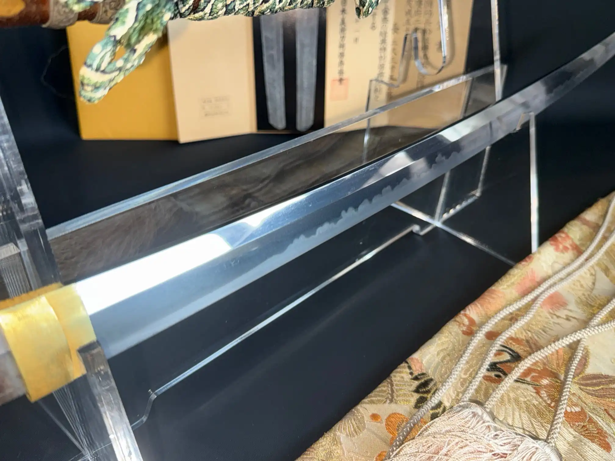 Close-up of a sharp Tachi Yokoyama Sukekane katana blade displaying its hamon on an acrylic stand