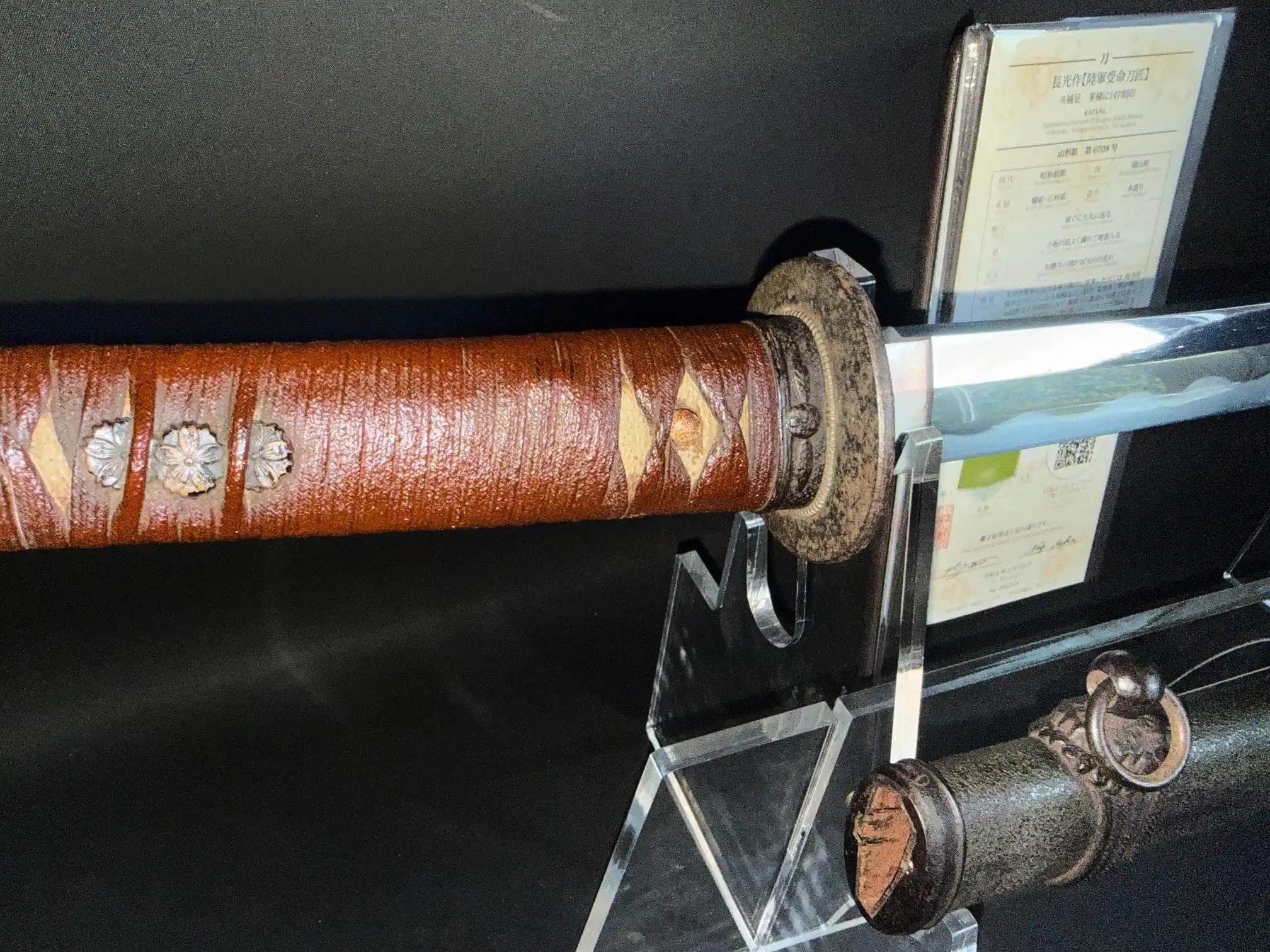 Close-up of a WWII Katana Ichihara Nagamitsu's brown-wrapped tsuka and blade, with paper display