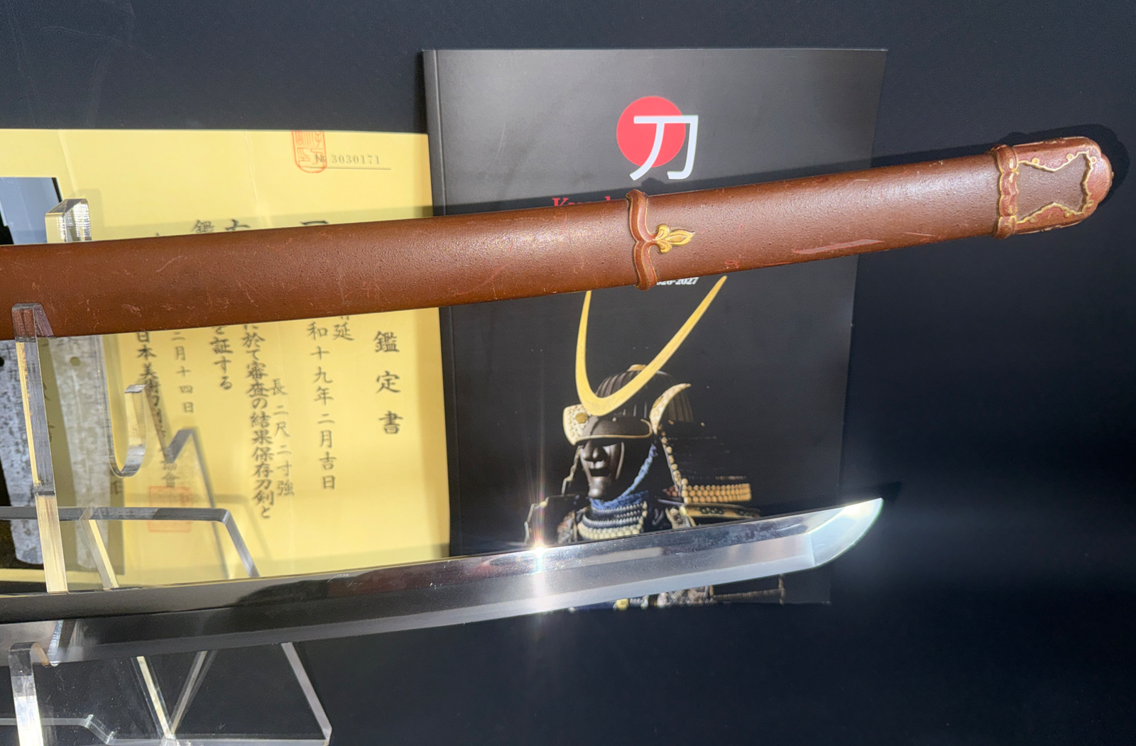 Close-up of a Yasukuni Gendaitō Yasunobu katana and scabbard on a stand with paperwork