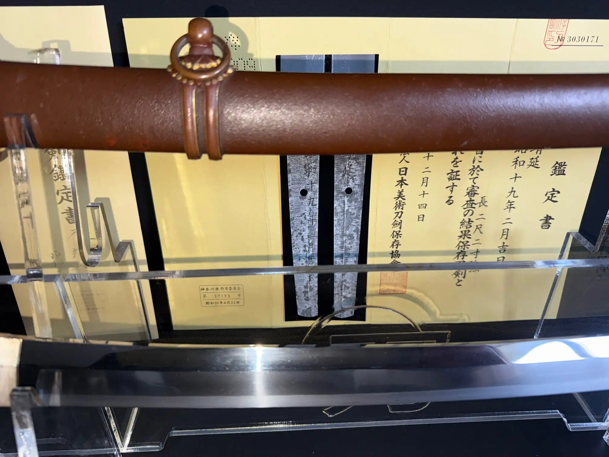 Close-up of a Yasukuni Gendaito Yasunobu katana and its brown Type 98 sheath on a stand with paperwork