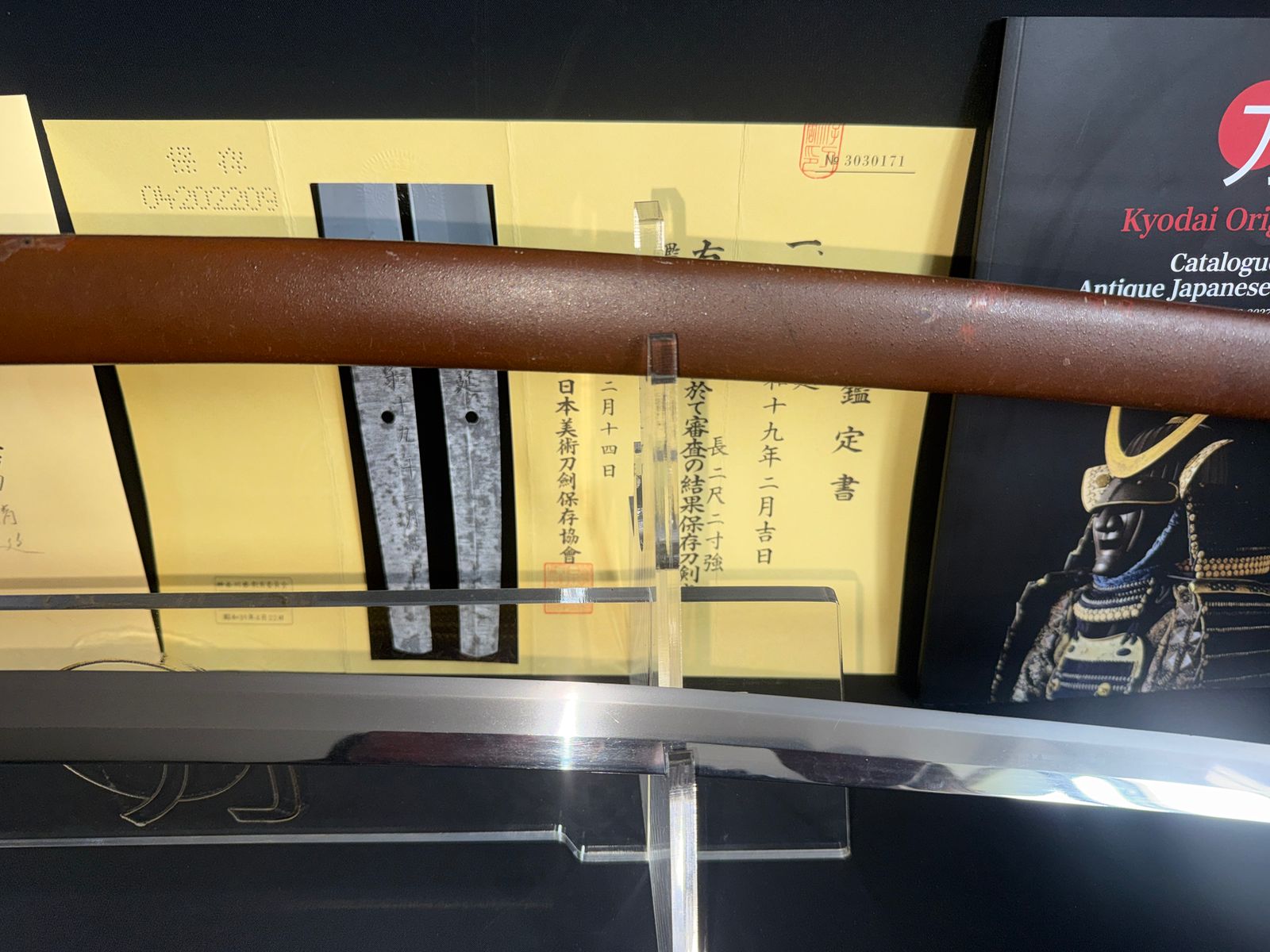 Close-up, top-down view of Yasukuni Gendaitō Yasunobu Katana and scabbard with Japanese calligraphy behind.