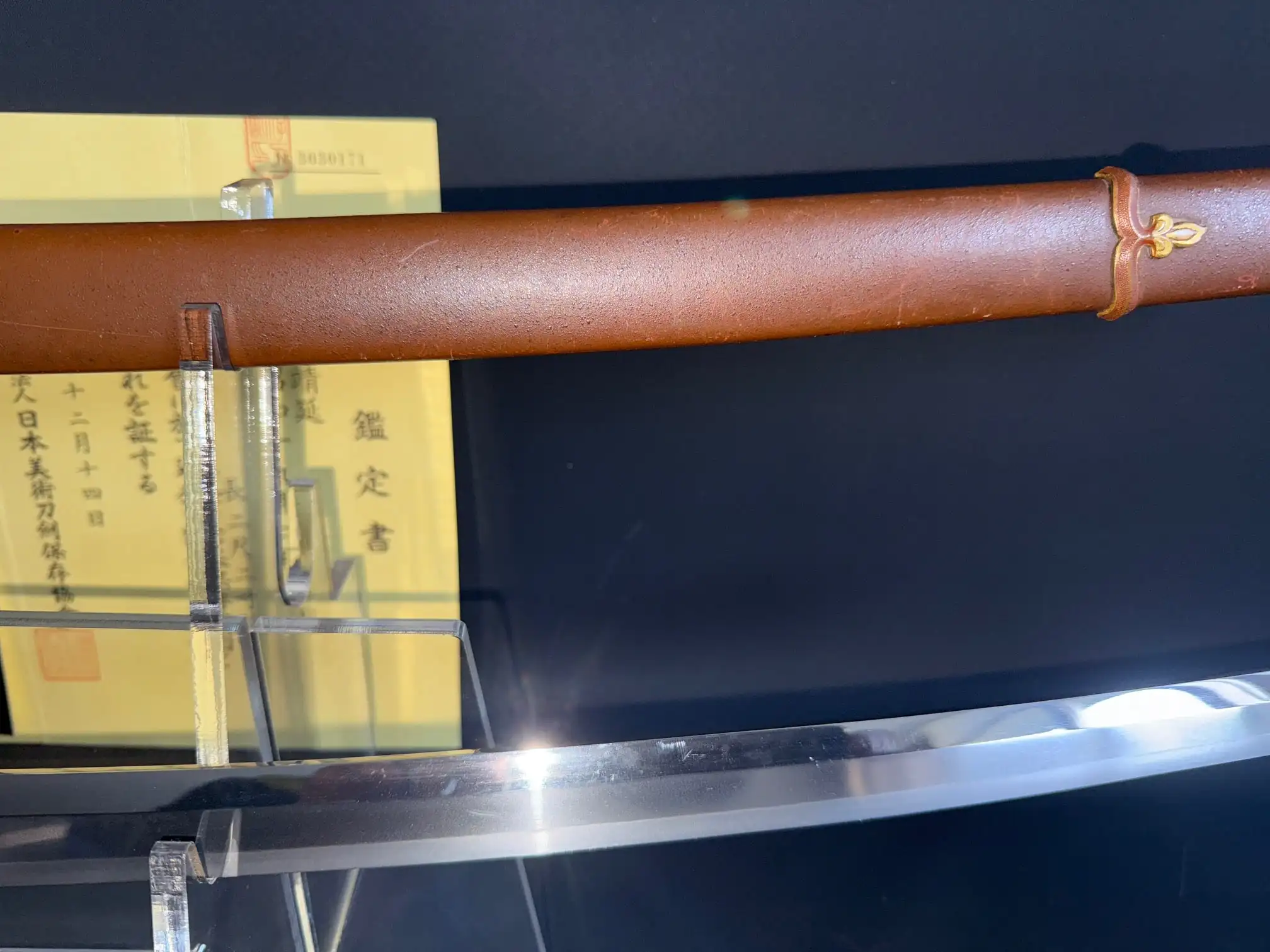 Polished Yasukuni Gendaito Yasunobu katana blade emerging from its brown saya, certification behind