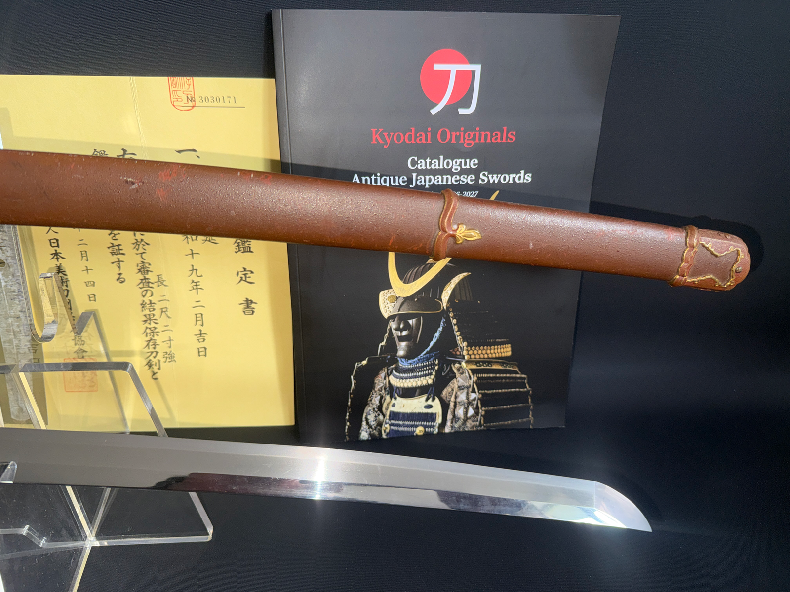 A Kyodai Originals Yasukuni Gendaito Yasunobu katana, with its brown scabbard and polished blade, alongside certificates.