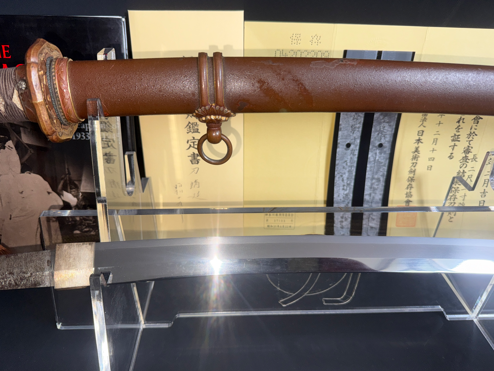 Close-up of a Yasukuni Gendaitō Yasunobu katana, showing the brown saya and silver blade in a stand