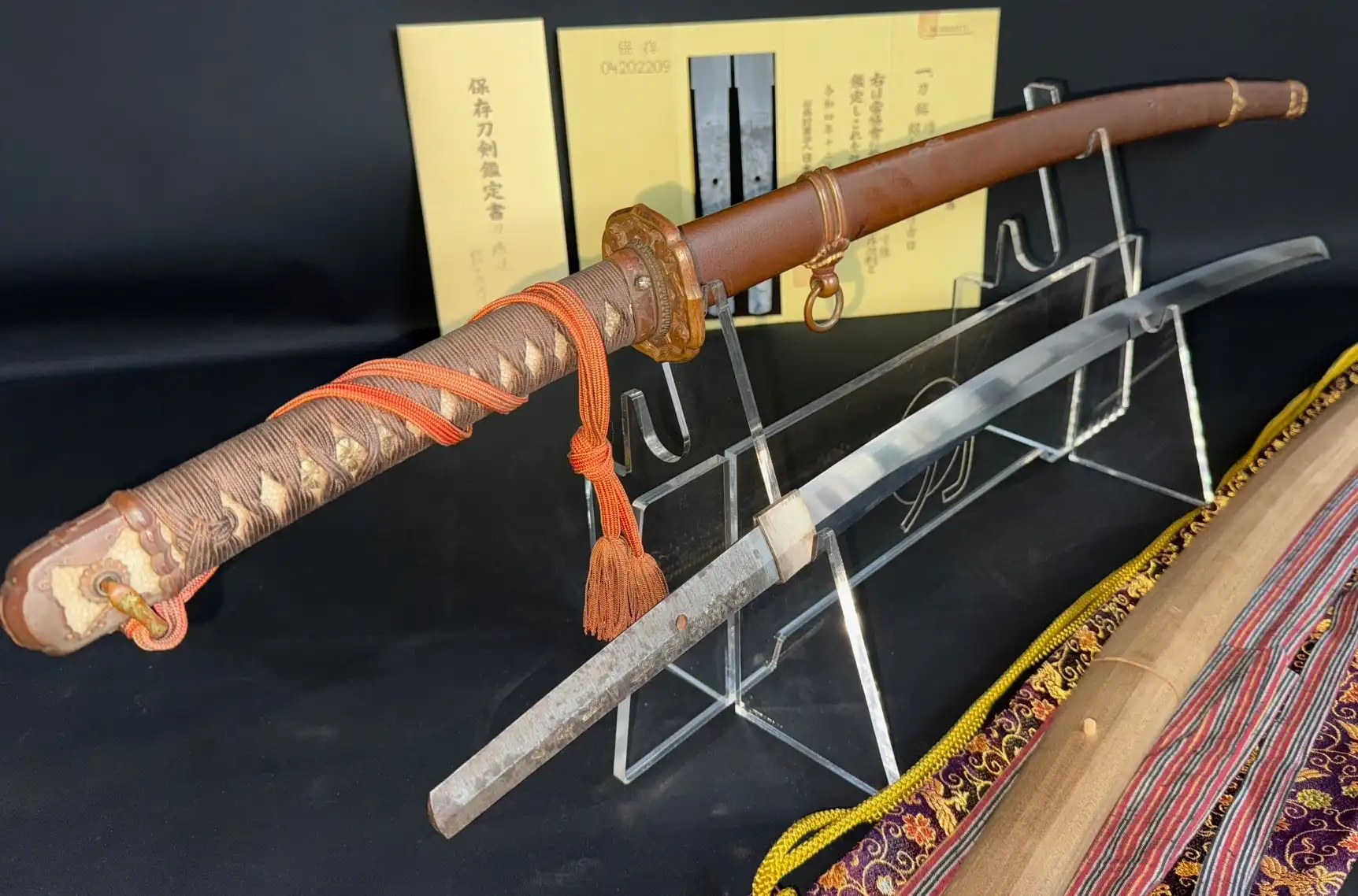 Yasunobu Yasukuni Gendaito katana with scabbard, blade exposed, and paperwork on a black background