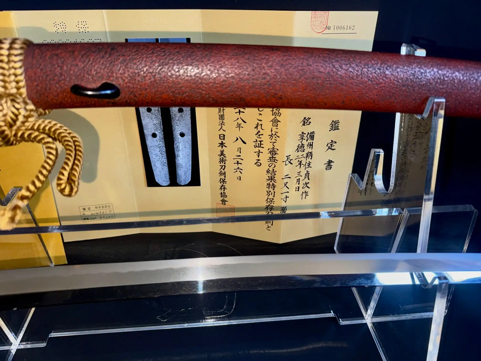 Katana Bishū Tomo-jū Sadatsugu, bright polished blade on stand next to scabbard and authenticity documents
