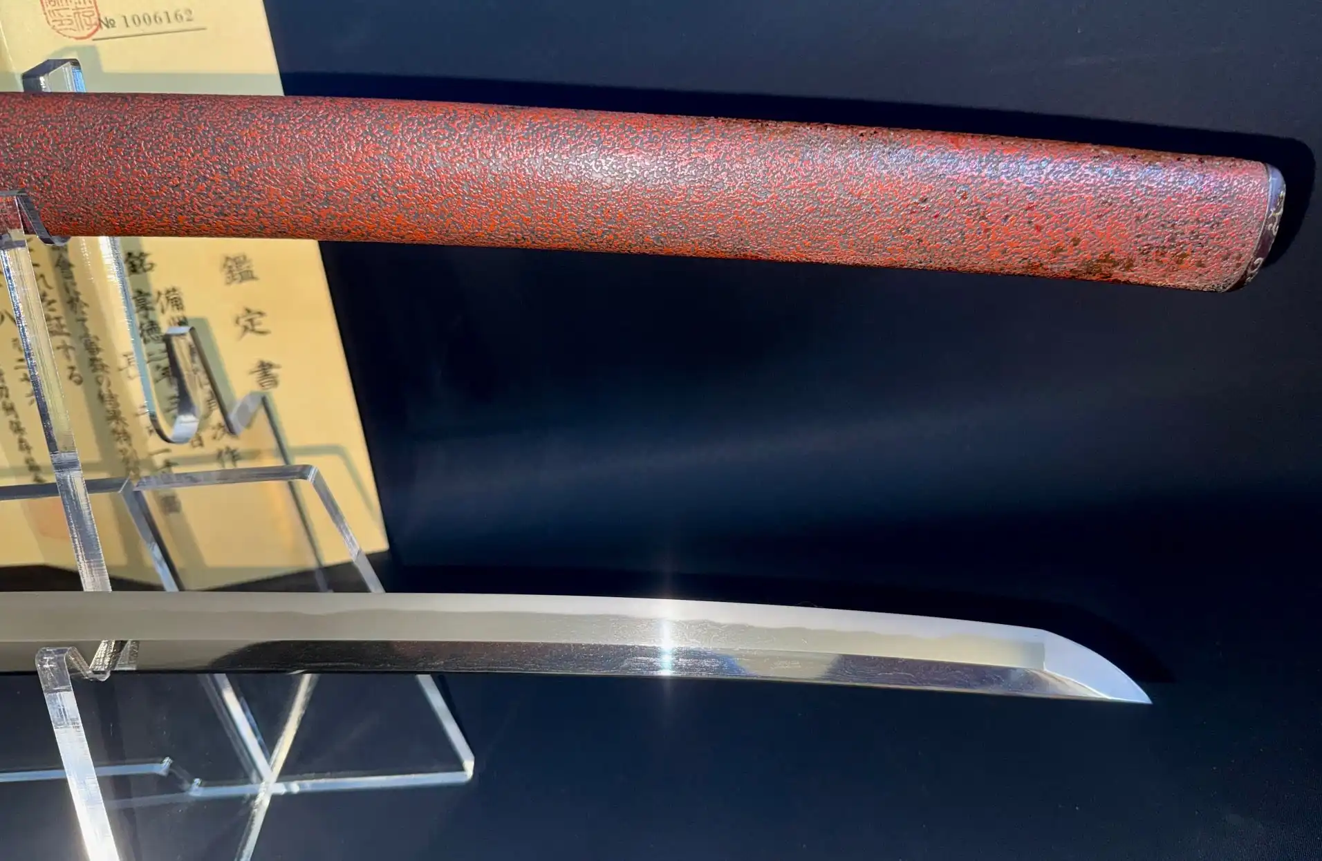 Katana Bishū Tomo-jū Sadatsugu, a close-up of the bright blade and textured red saya, on a stand