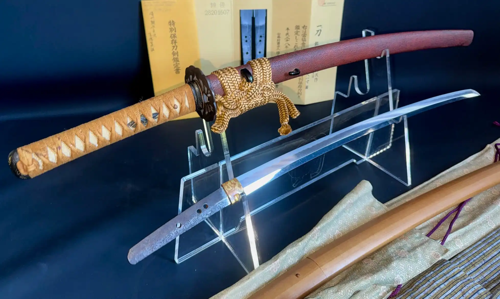 Katana Bishū Tomo-jū Sadatsugu, blade out of sheath, hilt with tan wrap and golden rope on stand
