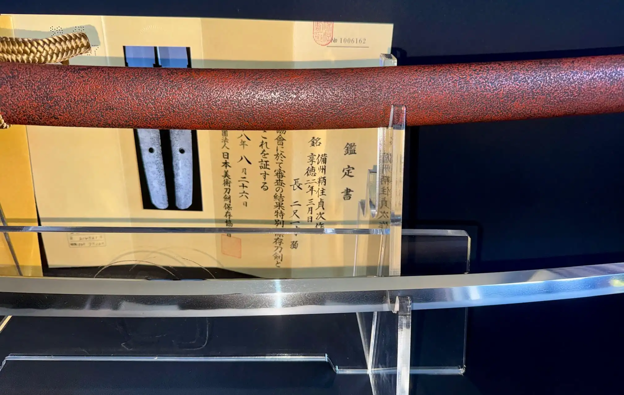 Katana Bishū Tomo-jū Sadatsugu, polished blade on stand, with red saya and certificate in background