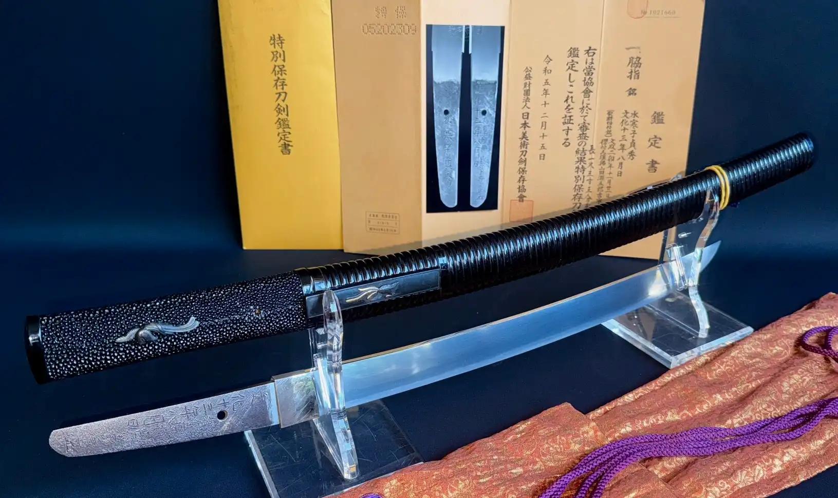 Suishinshi Masahide Wakizashi, black tsuka with textured rayskin and silver menuki, displayed with scabbard and papers.