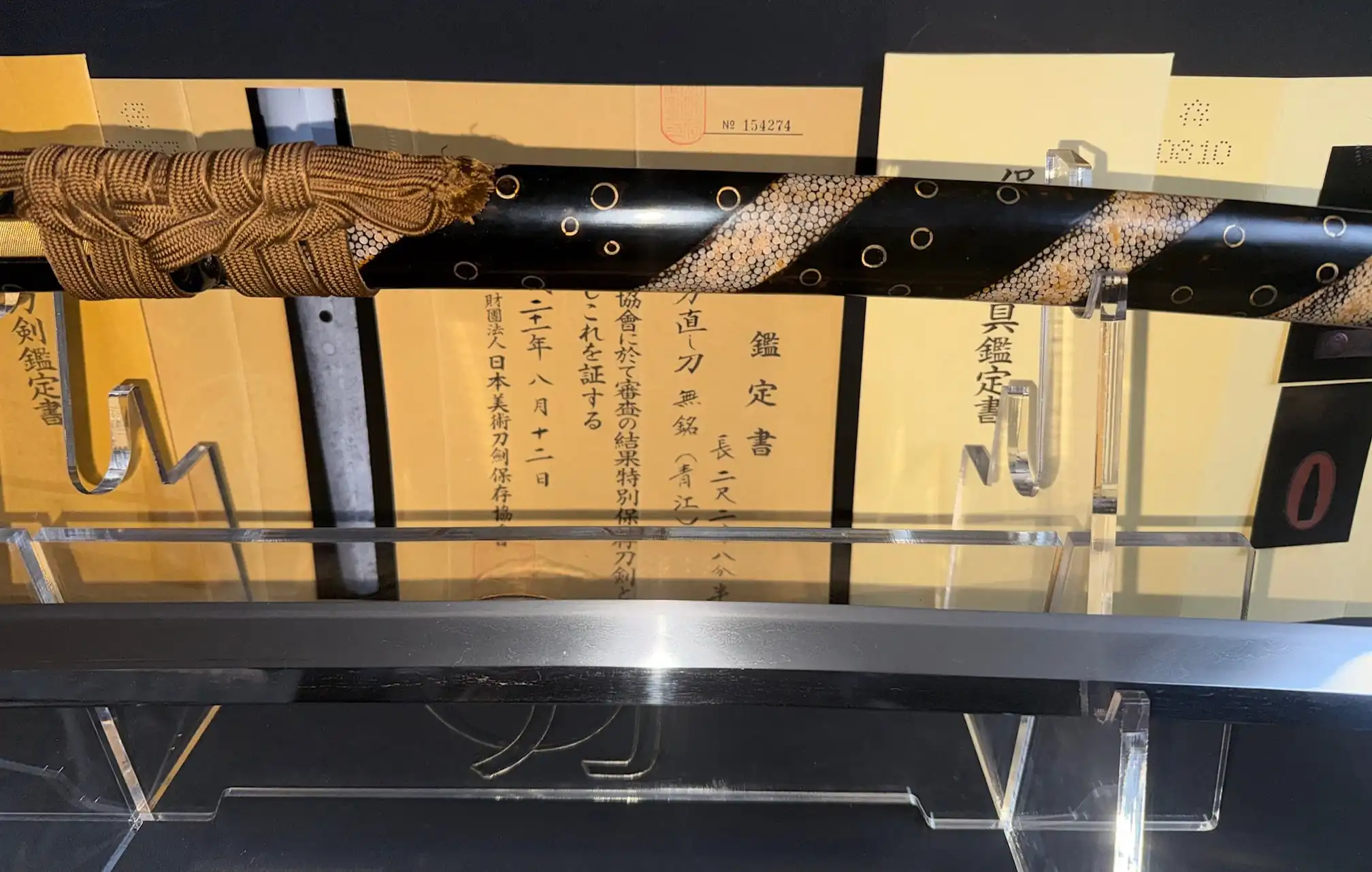 Aoe Nagamaki-Naoshi Katana with decorative black saya on display, Japanese papers behind.
