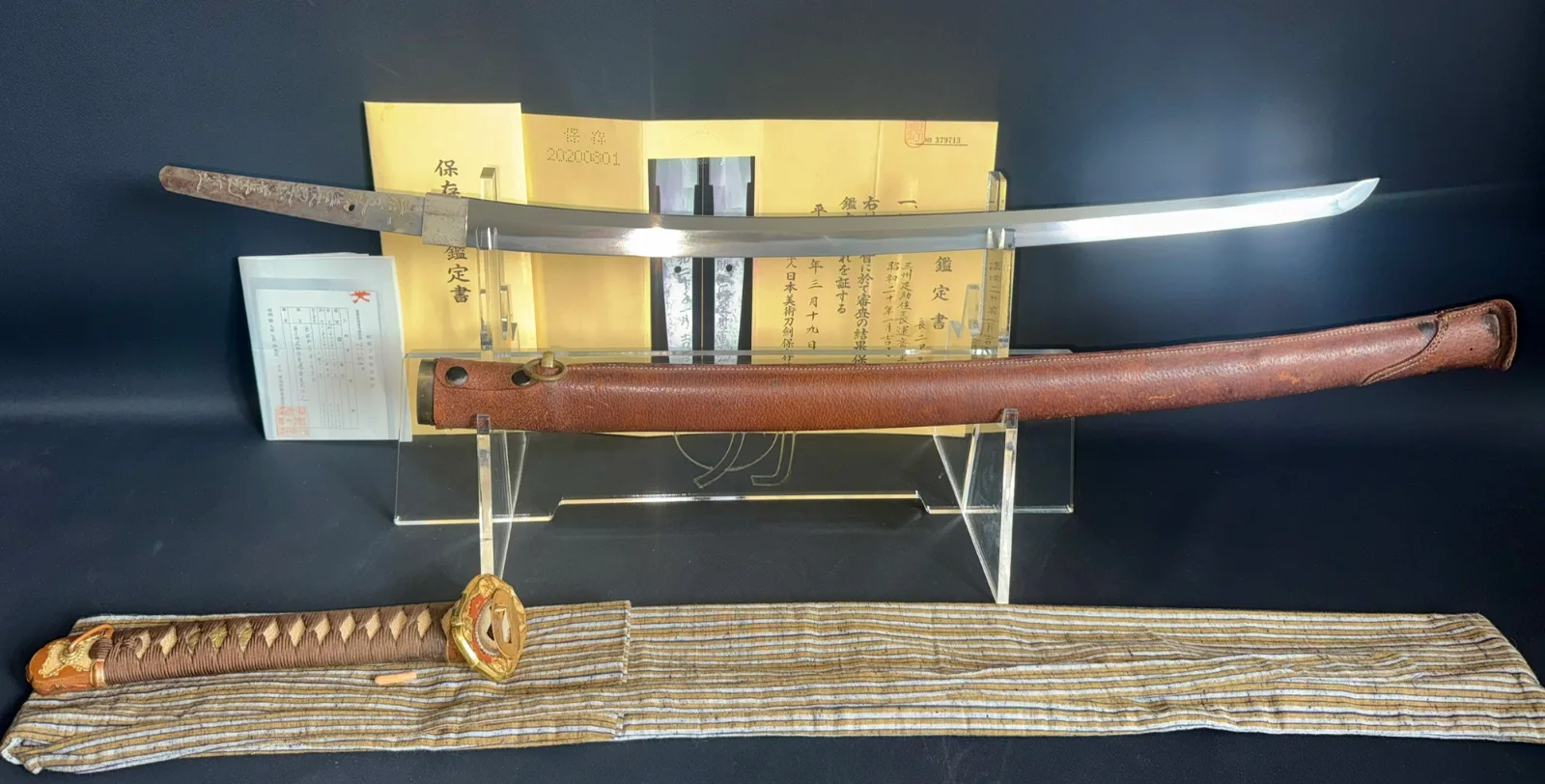 Chōunsai Shigemitsu katana 1945, blade and brown leather saya displayed horizontally with written certifications