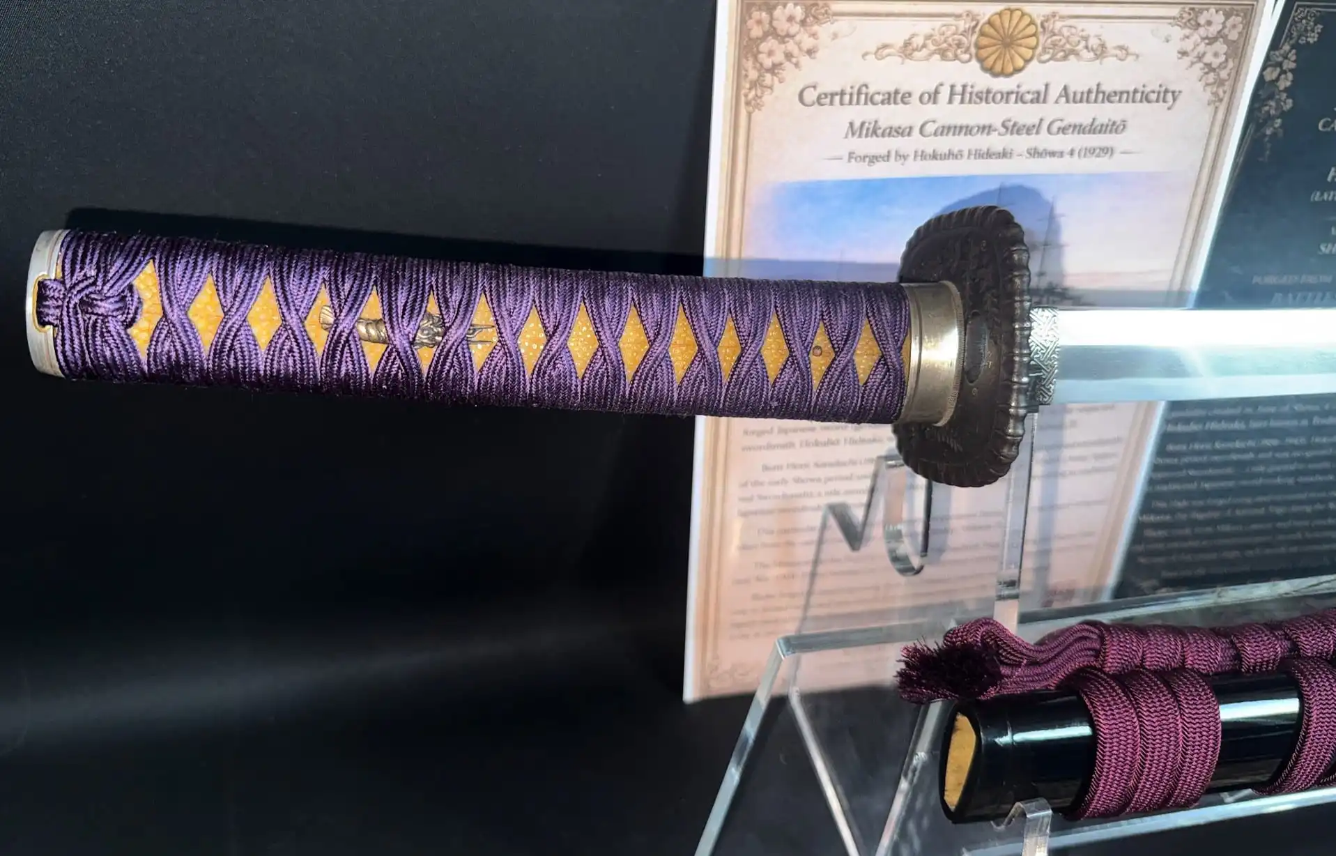 Close-up of Gendaitō Battleship Mikasa katana handle showing purple ito and certificate of authenticity