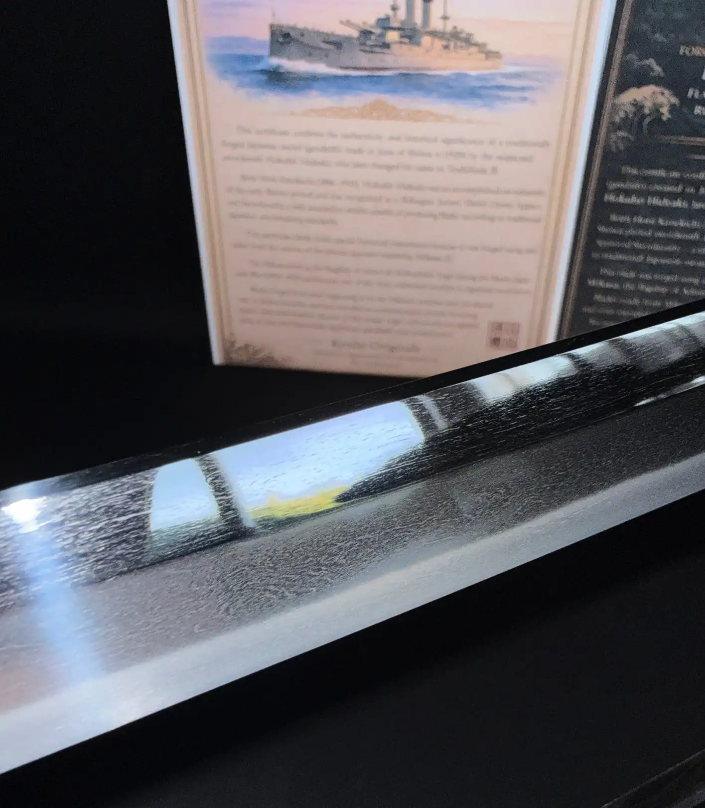 Close-up of a Katana Gendaitō Battleship Mikasa blade, showing the distinctive steel grain with blurred certificates.