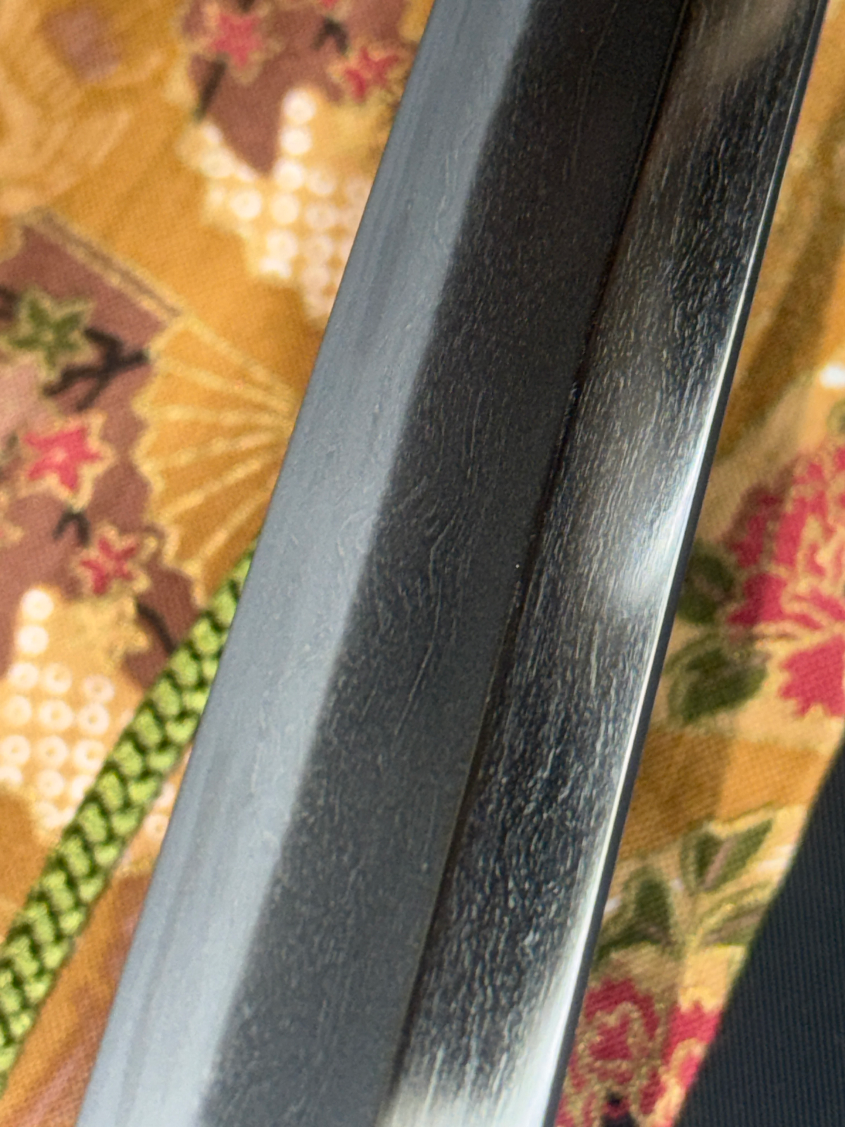 Close-up of a Gendaito Battleship Mikasa katana blade showing distinct grain pattern against a patterned textile