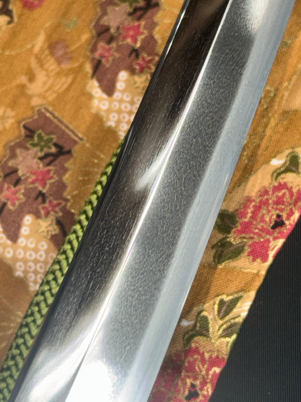 Close-up of a Gendaitō Battleship Mikasa katana blade showing its textured surface against patterned fabric.