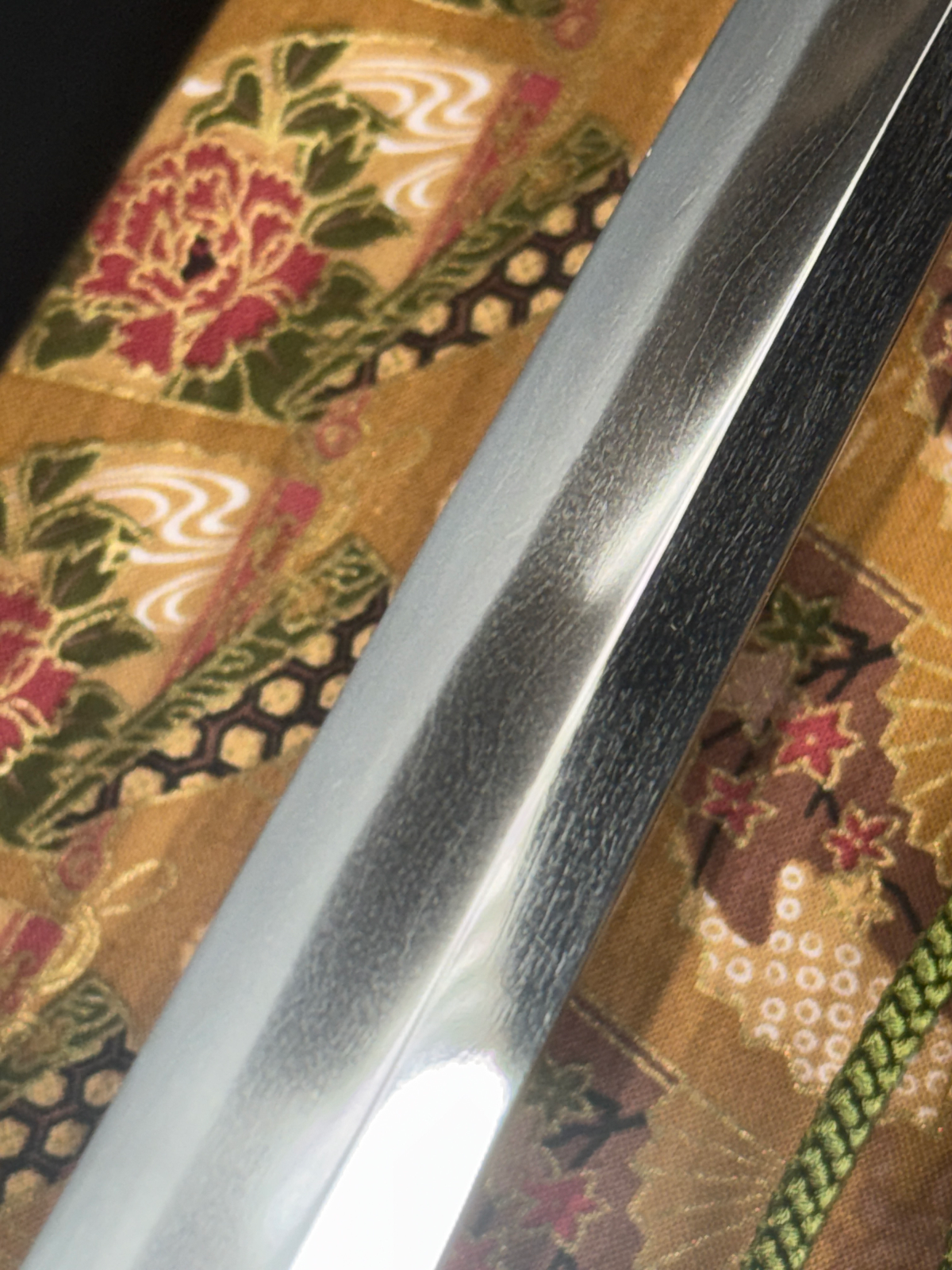 Close-up of a Gendaitō Battleship Mikasa katana blade showing hamon detail against vintage Japanese textile