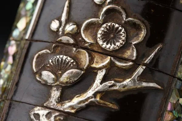 Close-up of an Edo Japanese Inro, an antique accessory, featuring delicate metalwork flowers and mother-of-pearl inlay.