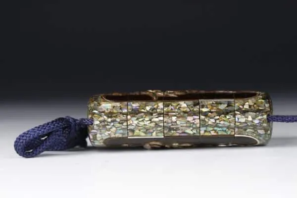 Edo Japanese Inro accessory, side view of intricate mother-of-pearl inlay and indigo cord against a dark background