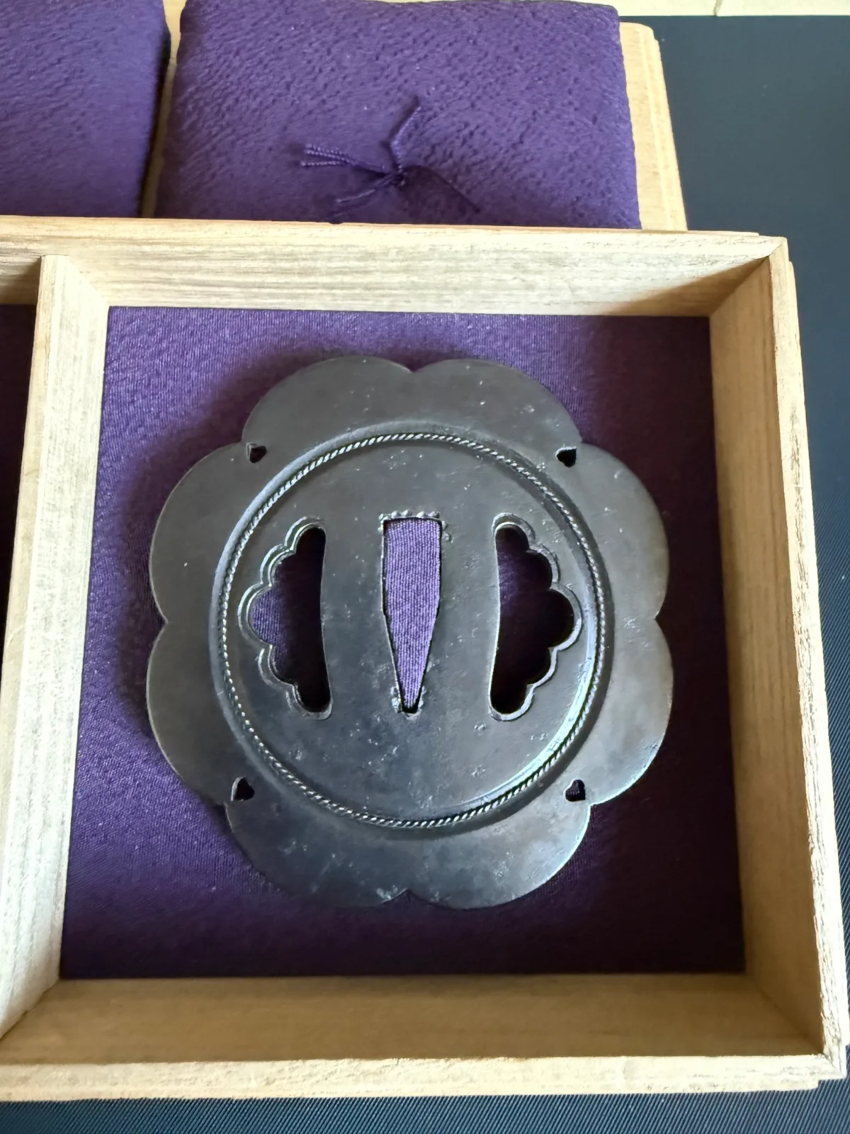 Kamiyoshi Fukanobu Daishō Tsuba Set, dark metal sword guard in wooden box on purple cloth, top view