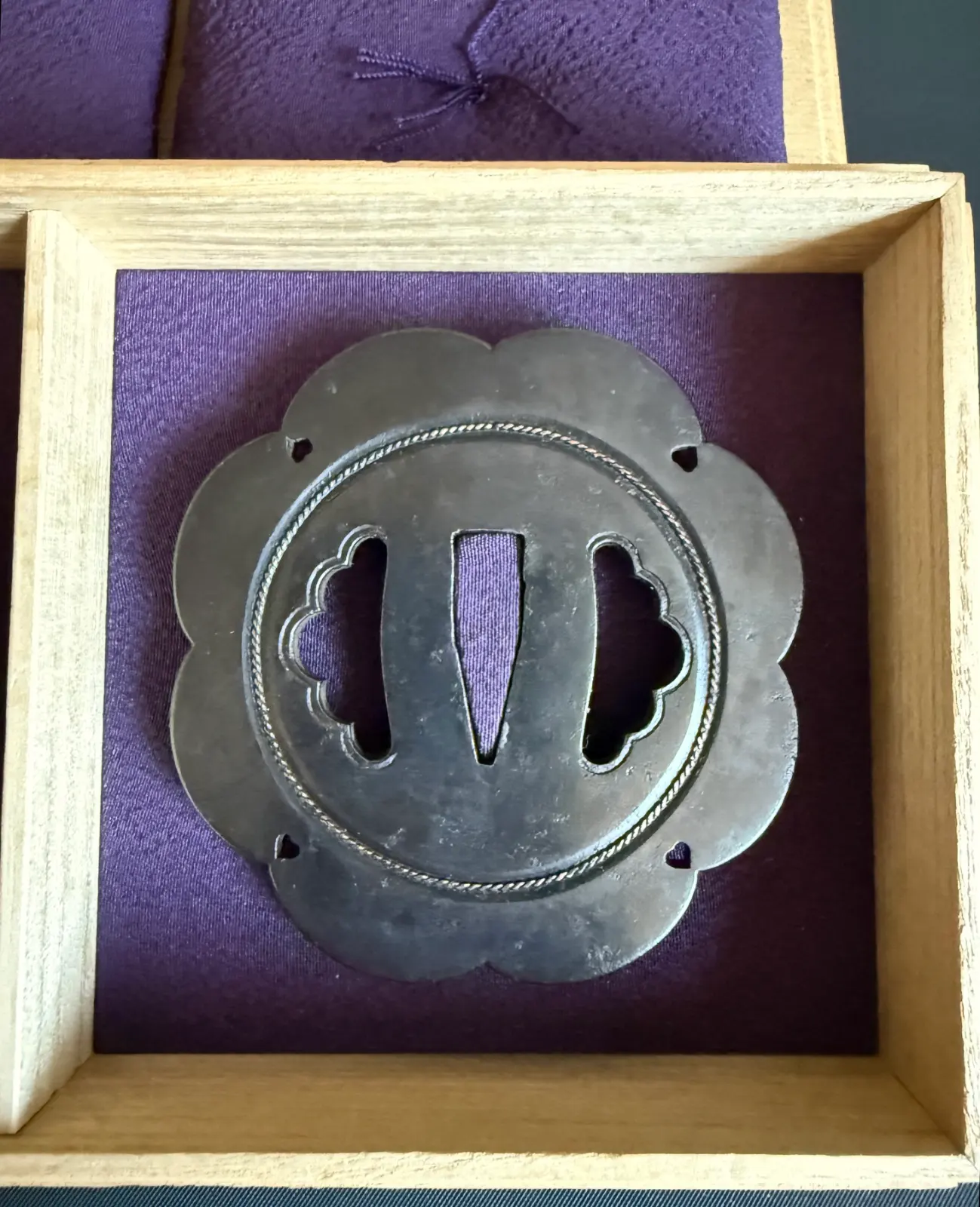Kamiyoshi Fukanobu Daishō Tsuba top view, intricate silver rope border on ornate metal sword guard in wooden box