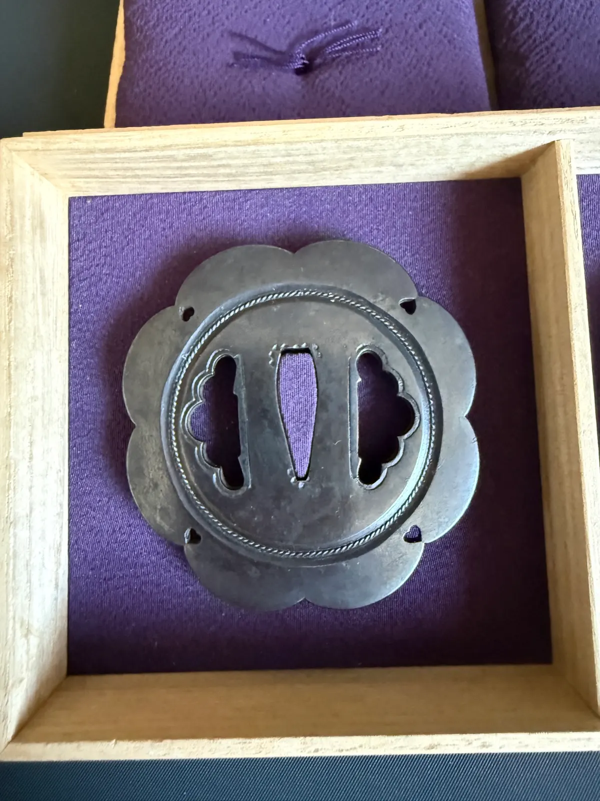 Kamiyoshi Fukanobu Daishō Tsuba in wooden box, scalloped edge, silver metal with rope-like detail, top-down view