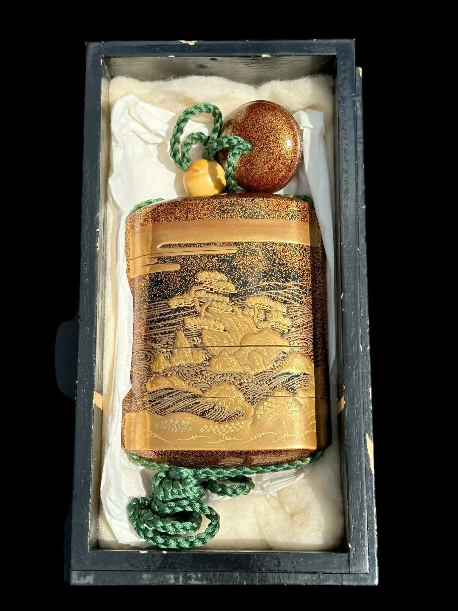 Top-down view of an Antique Inro 1840 Makie accessory in a wooden box, featuring gold landscapes on black Wajima lacquer