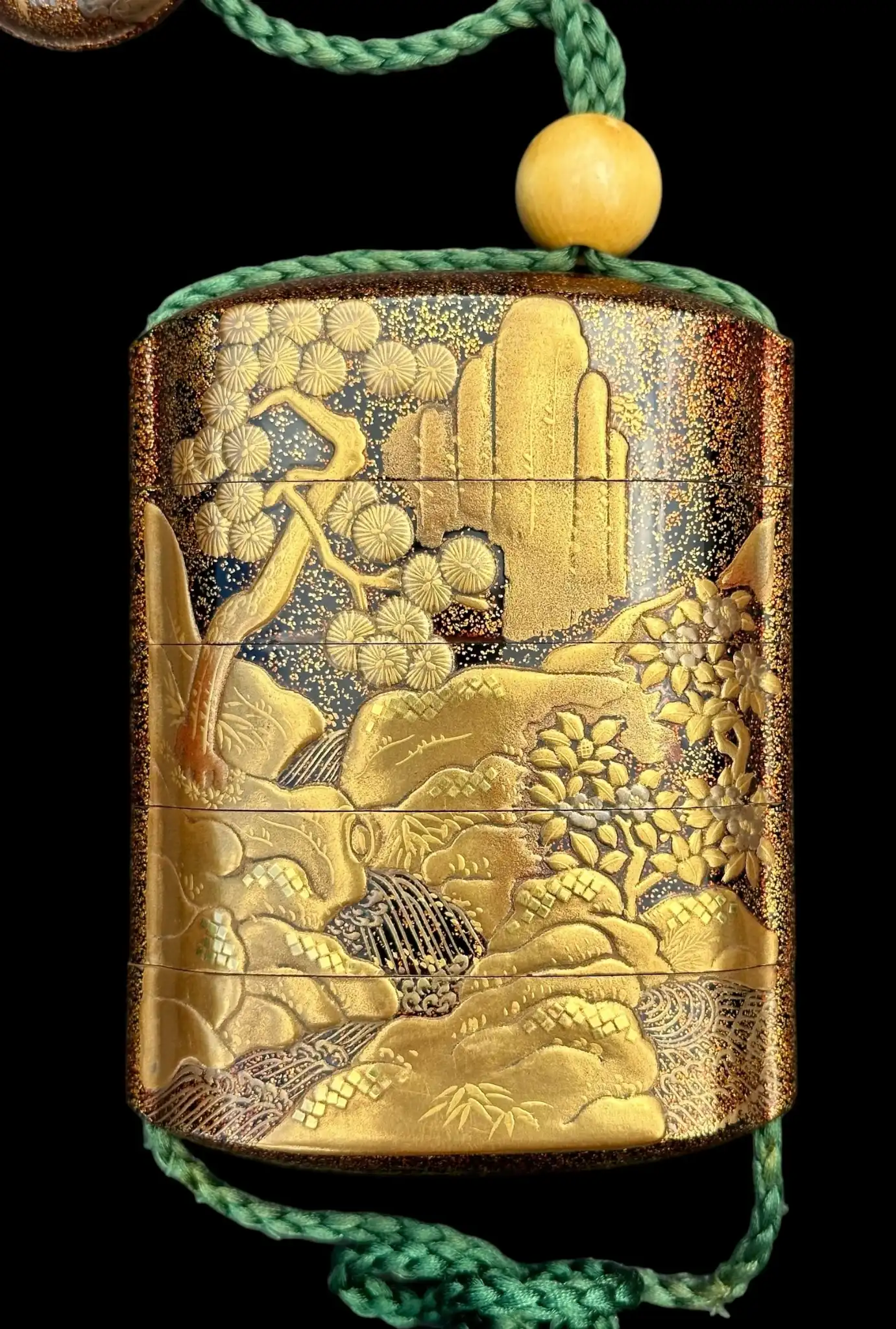 Close-up Antique Inro 1840 Makie accessory, a tiered lacquer box with intricate gold landscape artwork and green cord.