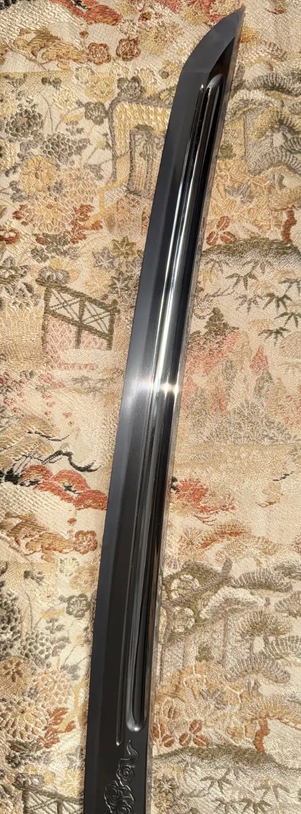 Close-up angle of the polished blade of a Suishinshi Masahide Wakizashi NBTHK Tokubetsu Hozon, showcasing its curvature and detailed carvings against a patterne