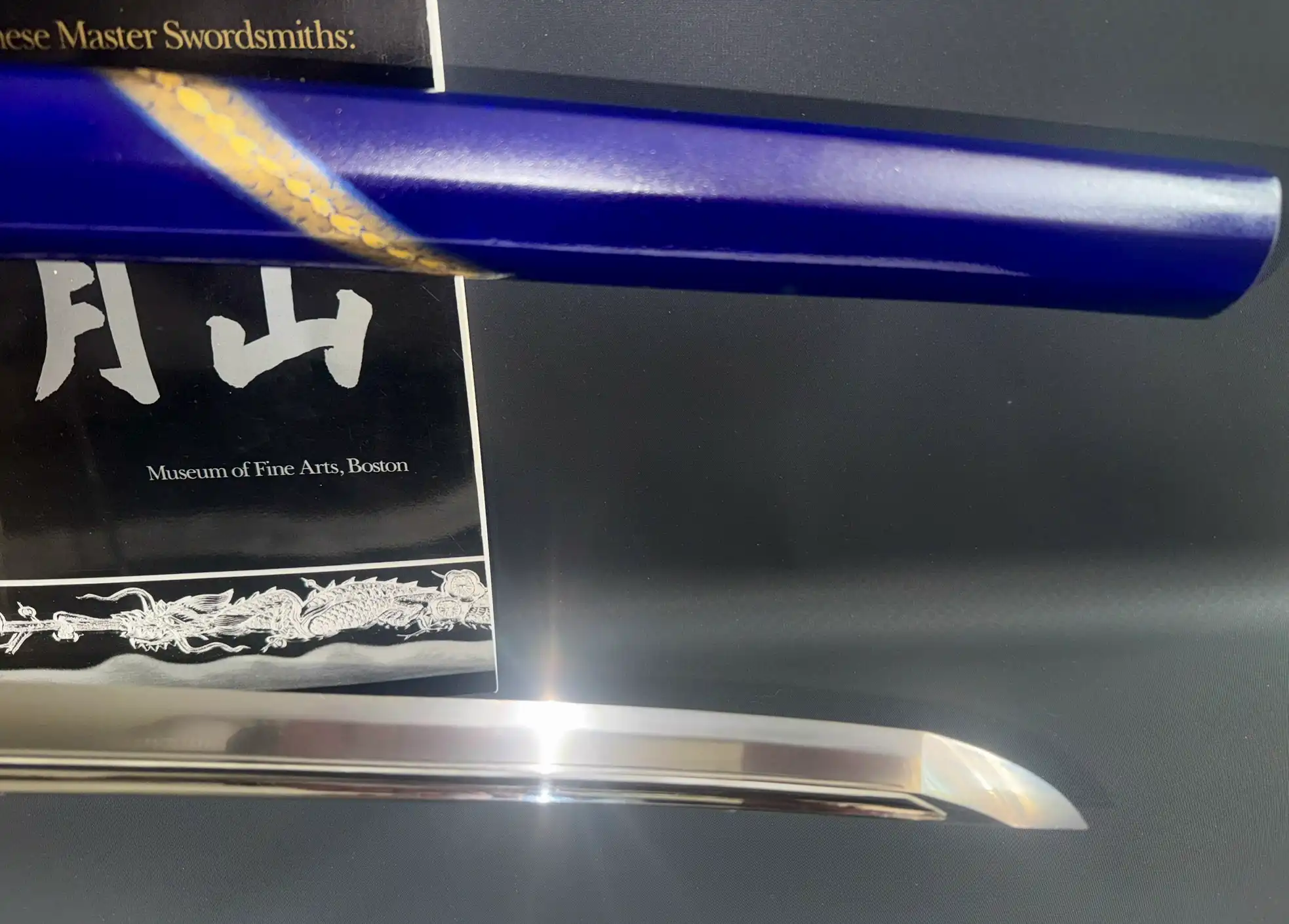 Blue saya with gold ornate detail over the polished blade of a Masterpiece Gassan Sadakazu katana.