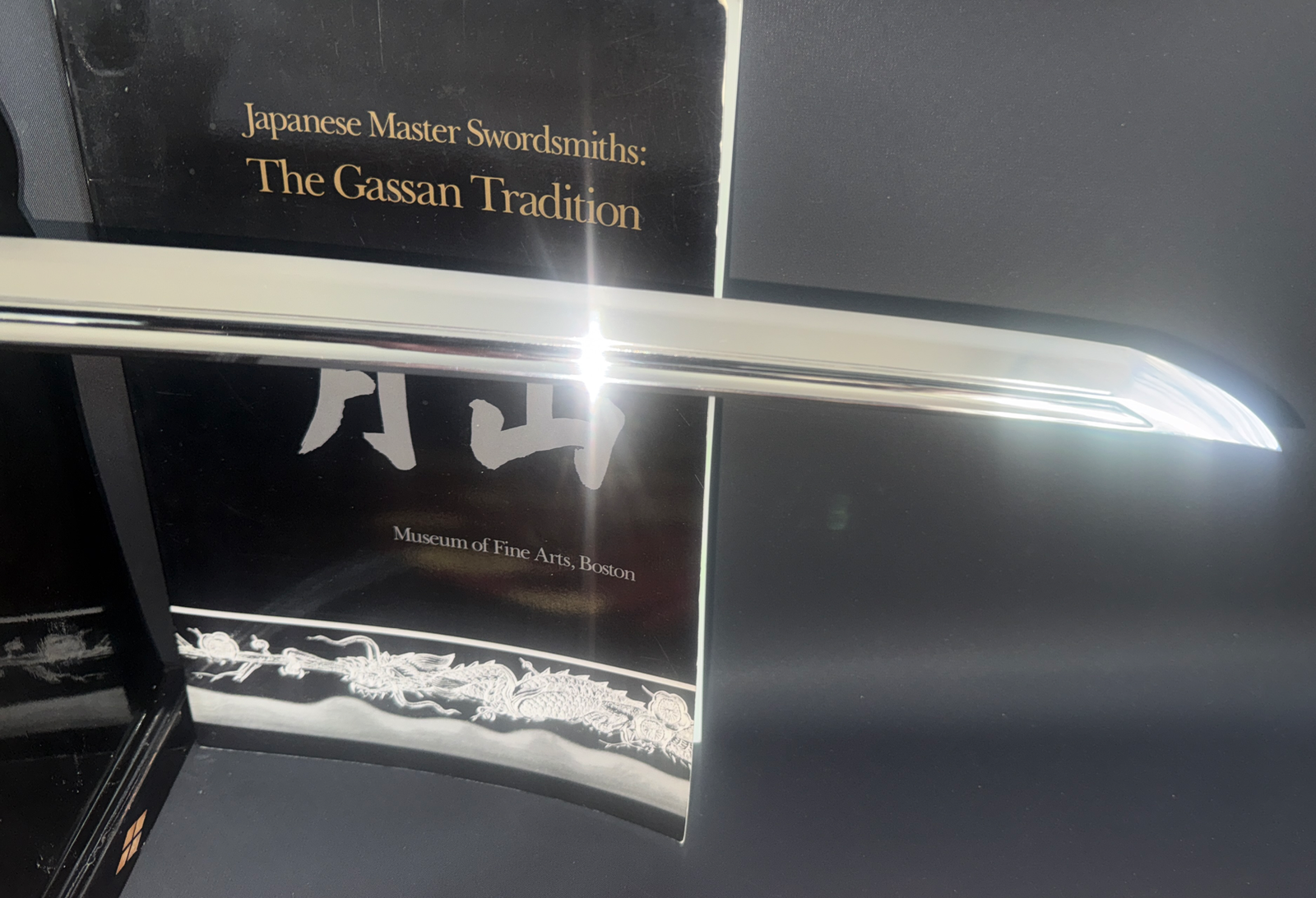 Shining Japanese Masterpiece Katana by Gassan Sadakazu blade reflected on "The Gassan Tradition" book, angled view
