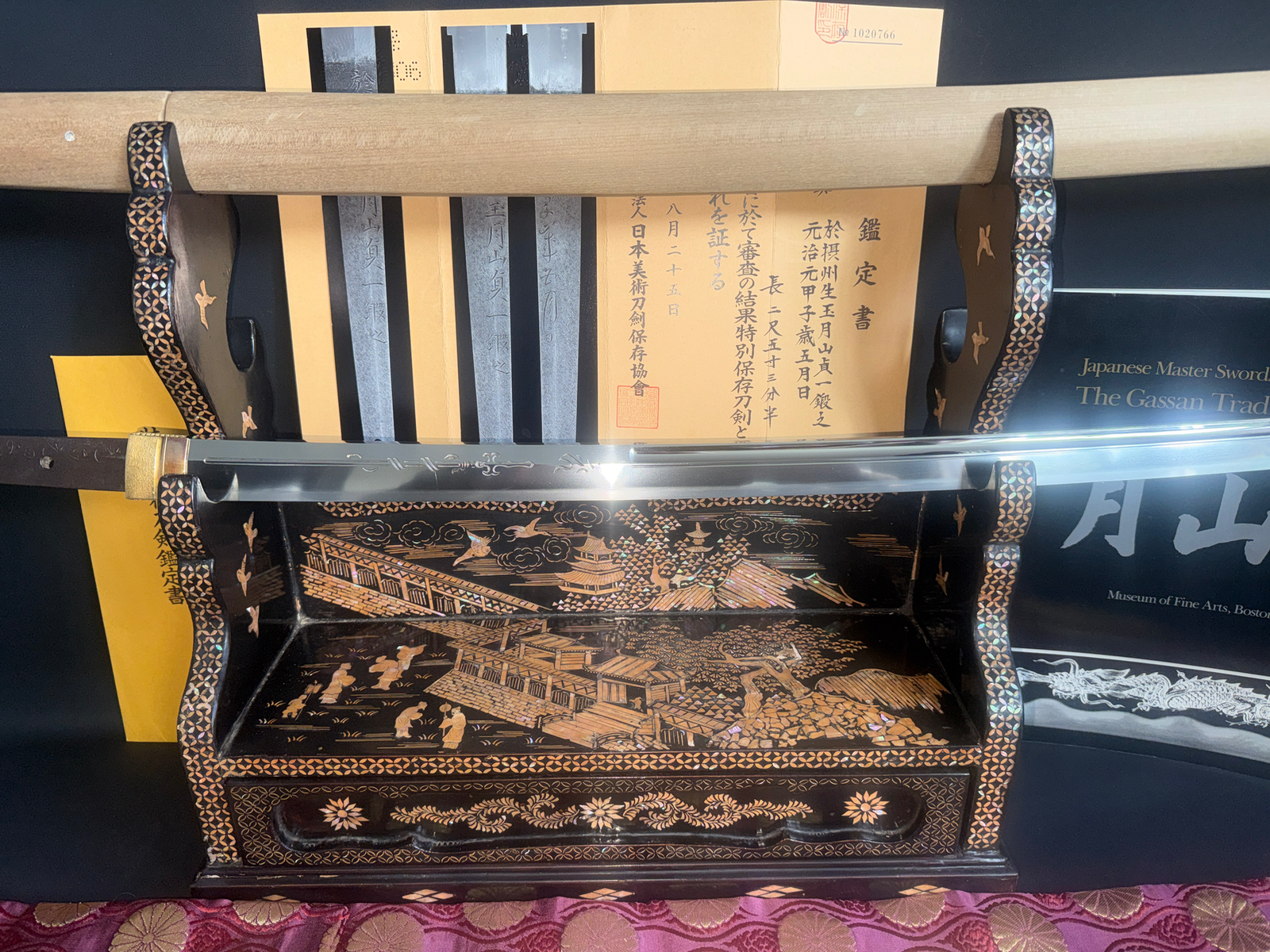 Japanese Masterpiece Katana by Gassan Sadakazu, displayed on an ornate stand with documentation and a book