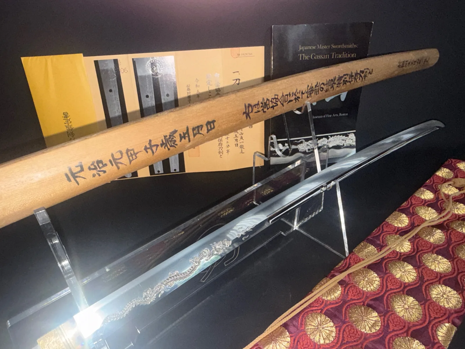 Angled Gassan Sadakazu Japanese Masterpiece Katana blade with horimono dragon, NBTHK papers, and wooden sword box.