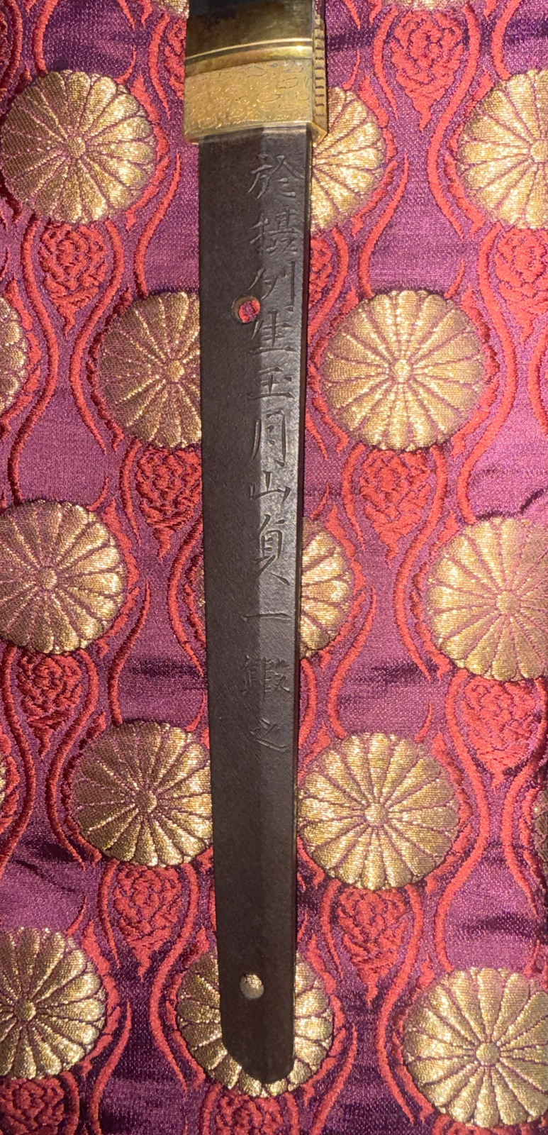 Nakago of Japanese Masterpiece Katana by Gassan Sadakazu, signed mei, on ornate purple and gold fabric.