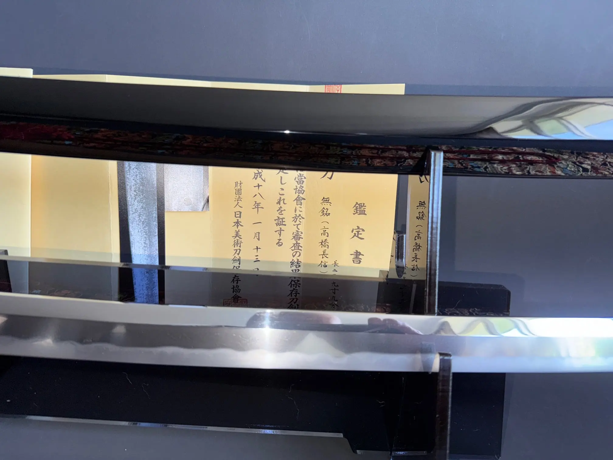 Close-up of Jinja Hōnō Tachi Naganobu Katana blade with hamon pattern and certification paperwork
