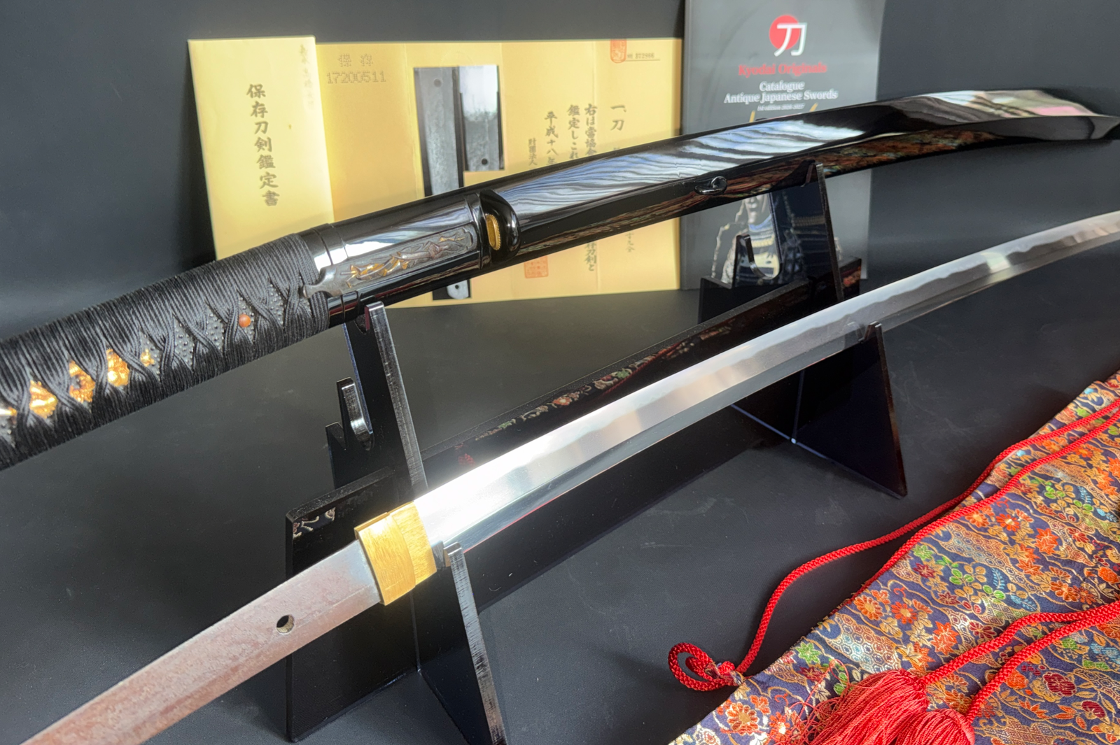 Jinja Hōnō Tachi Naganobu Katana display with polished blade and lacquered saya on stand, documents visible