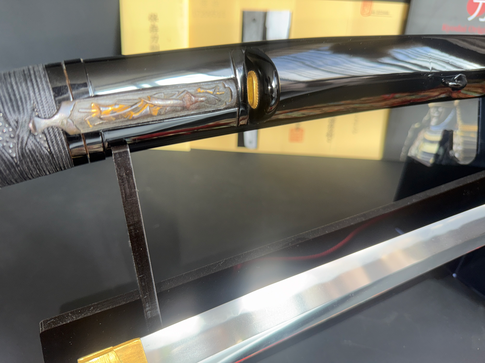 Close-up of Jinja Hōnō Tachi Naganobu katana in black saya with intricate menuki detail.