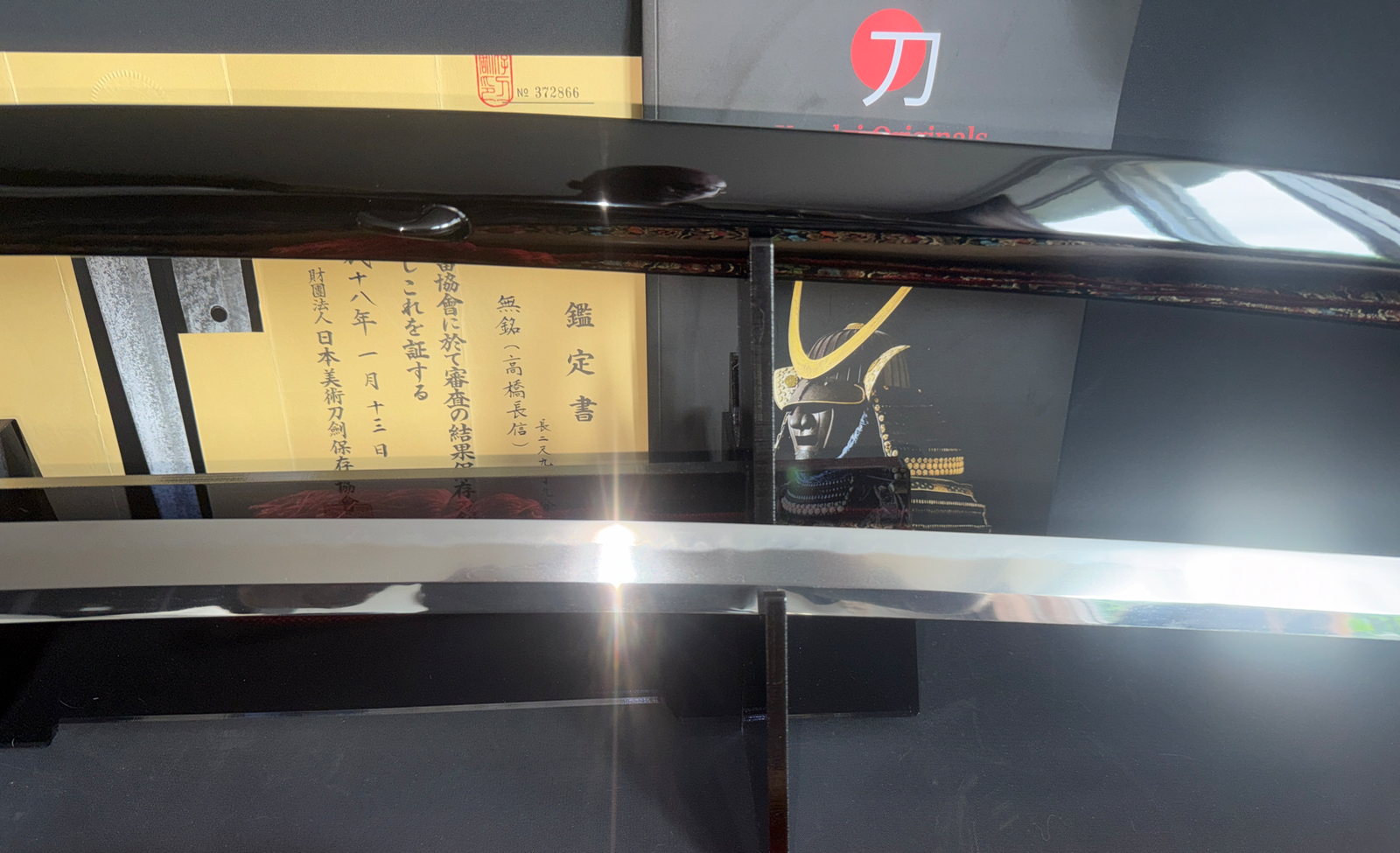 Reflective Jinja Hōnō Tachi Naganobu katana blade, shrine papers, and samurai helmet in background.